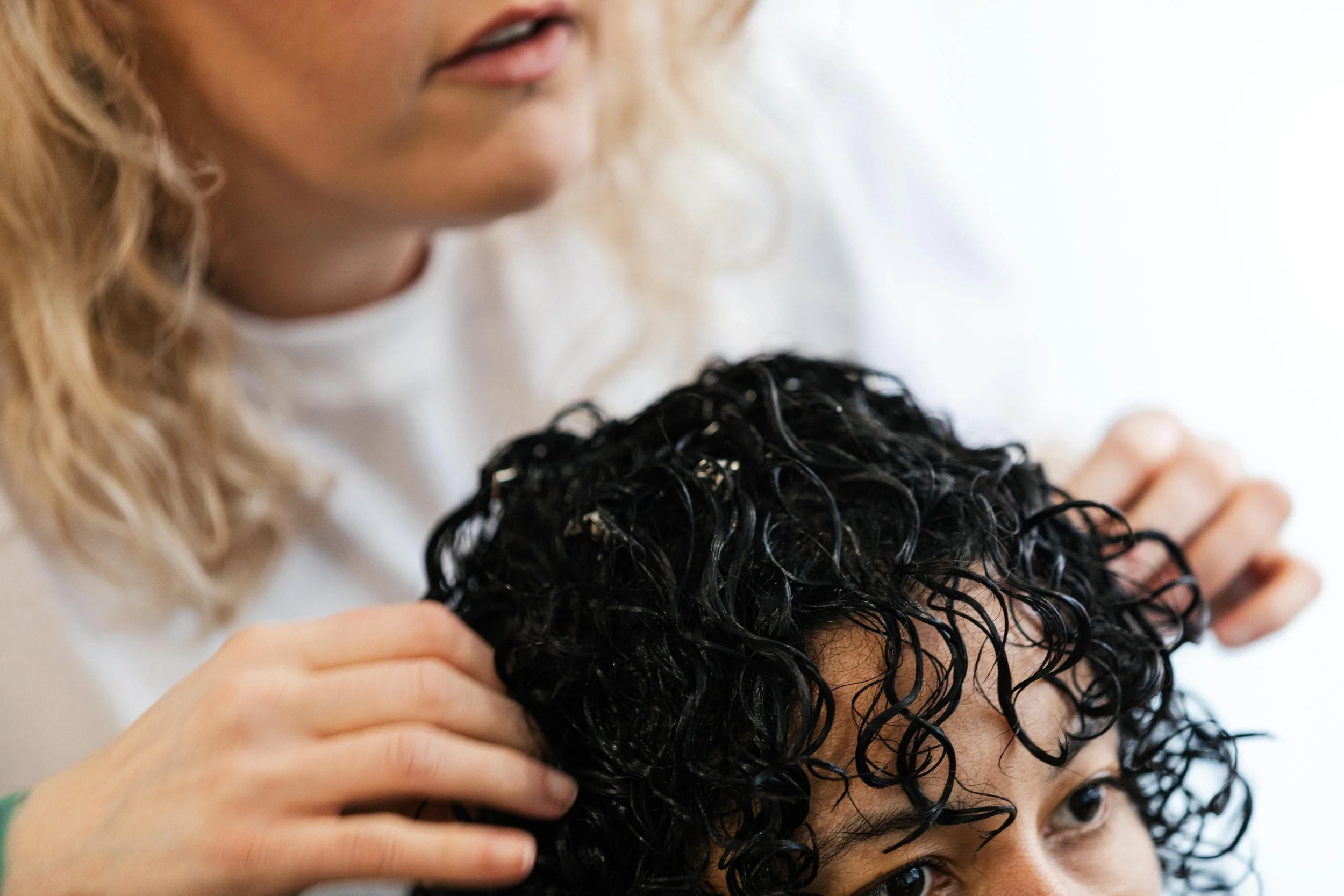 A hairdresser styling a person's curly black hair.