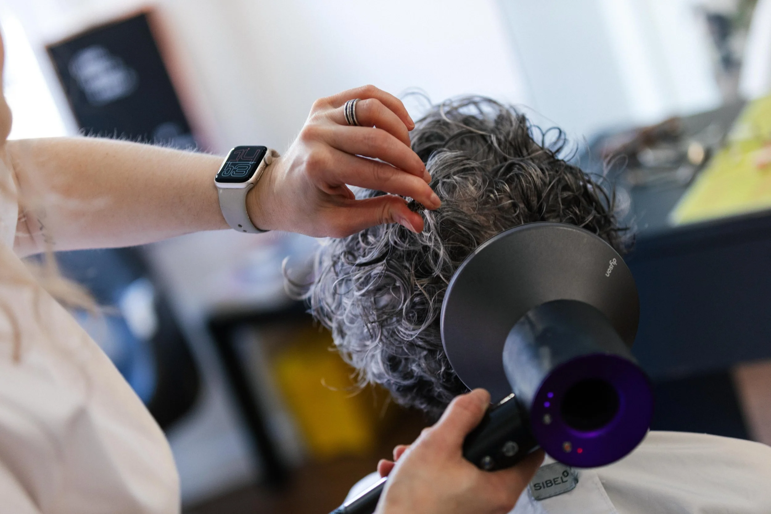 A person getting a haircut with a hair dryer, wearing a smartwatch on their wrist and a ring on their finger.