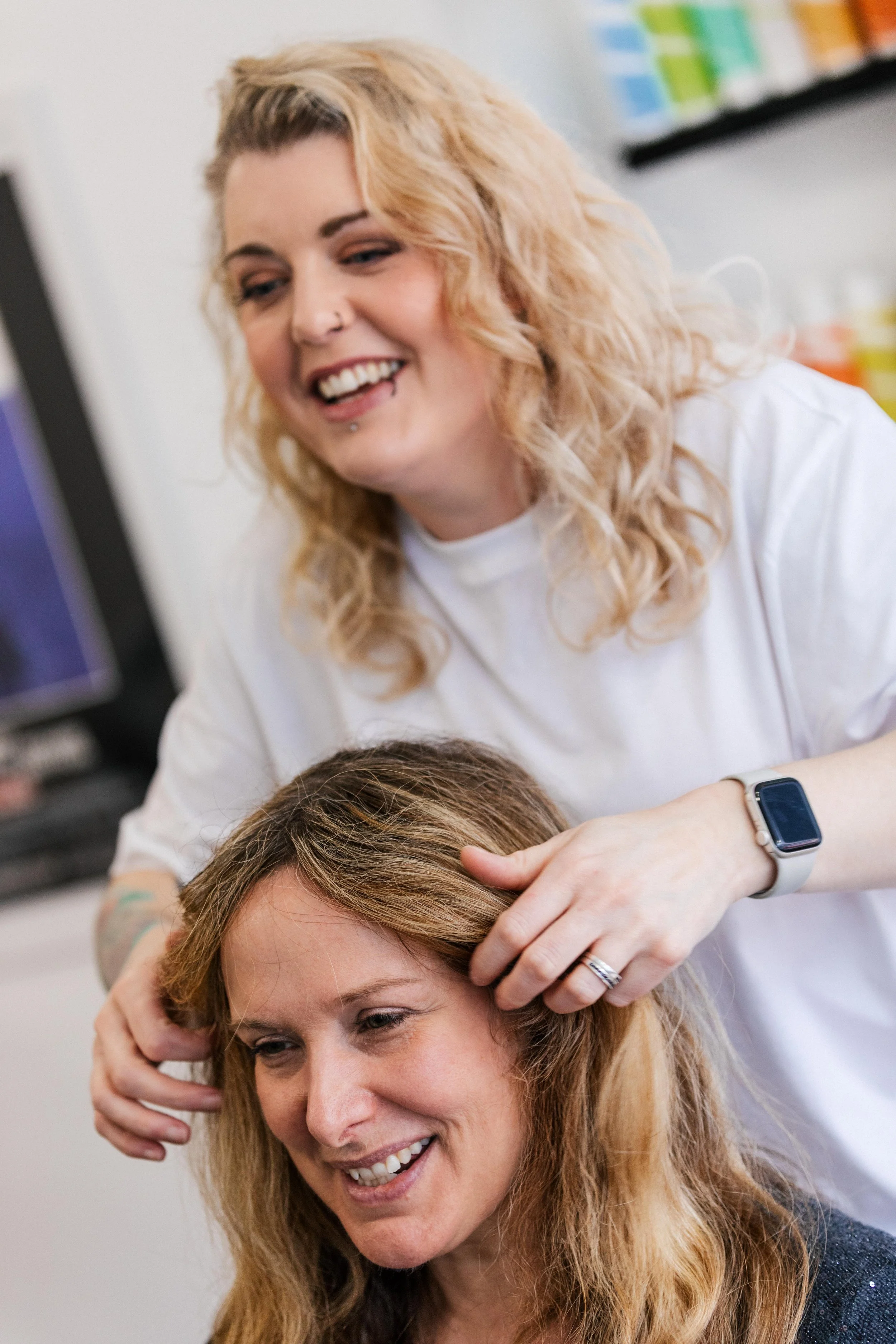 A woman with blond hair getting her hair played with by a stylist in a salon or similar setting.