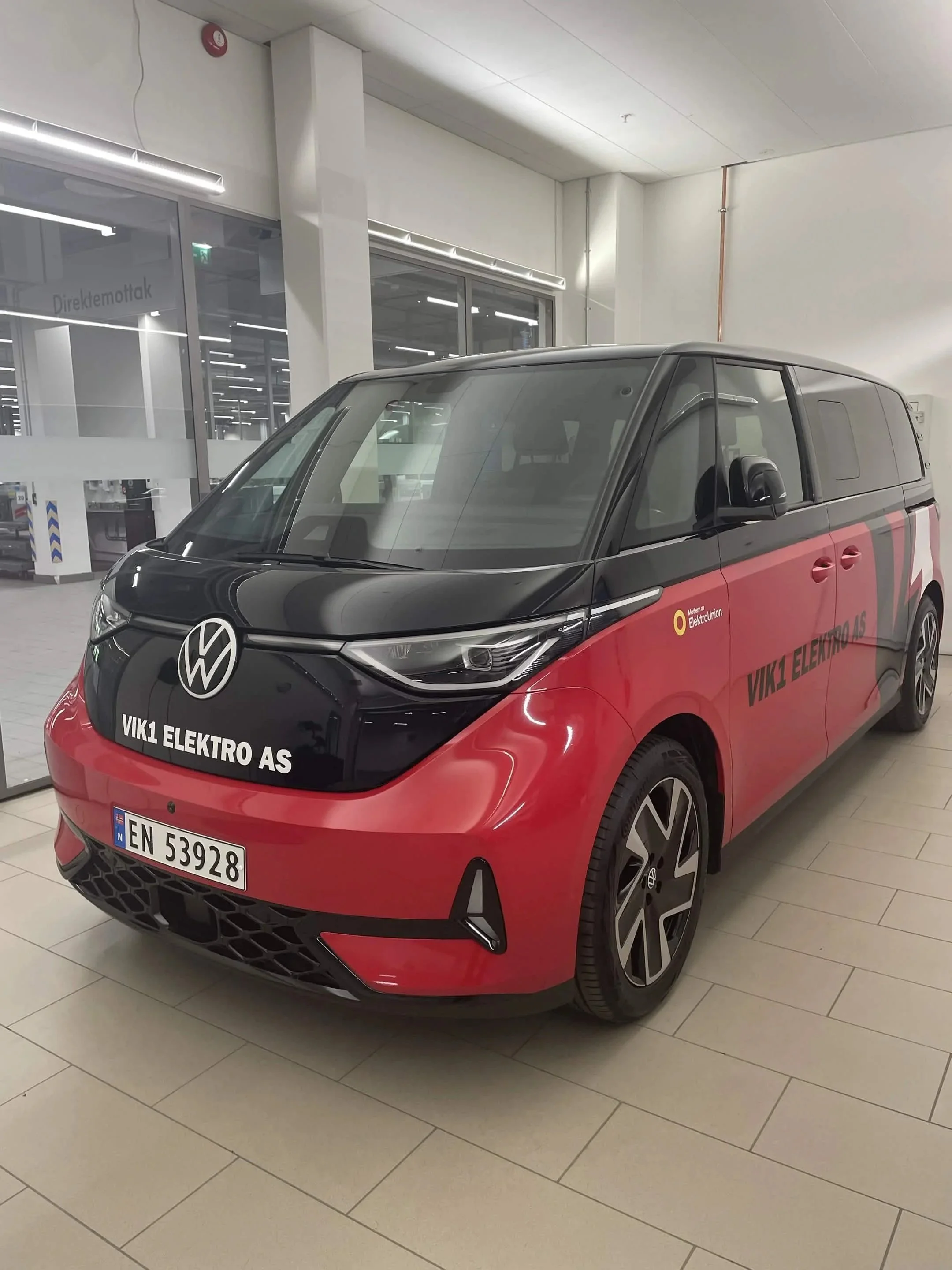 Elbil parkert innendørs med svart og rød farge, merket med VIK1 ELEKTRO AS, i nærheten av butikk.