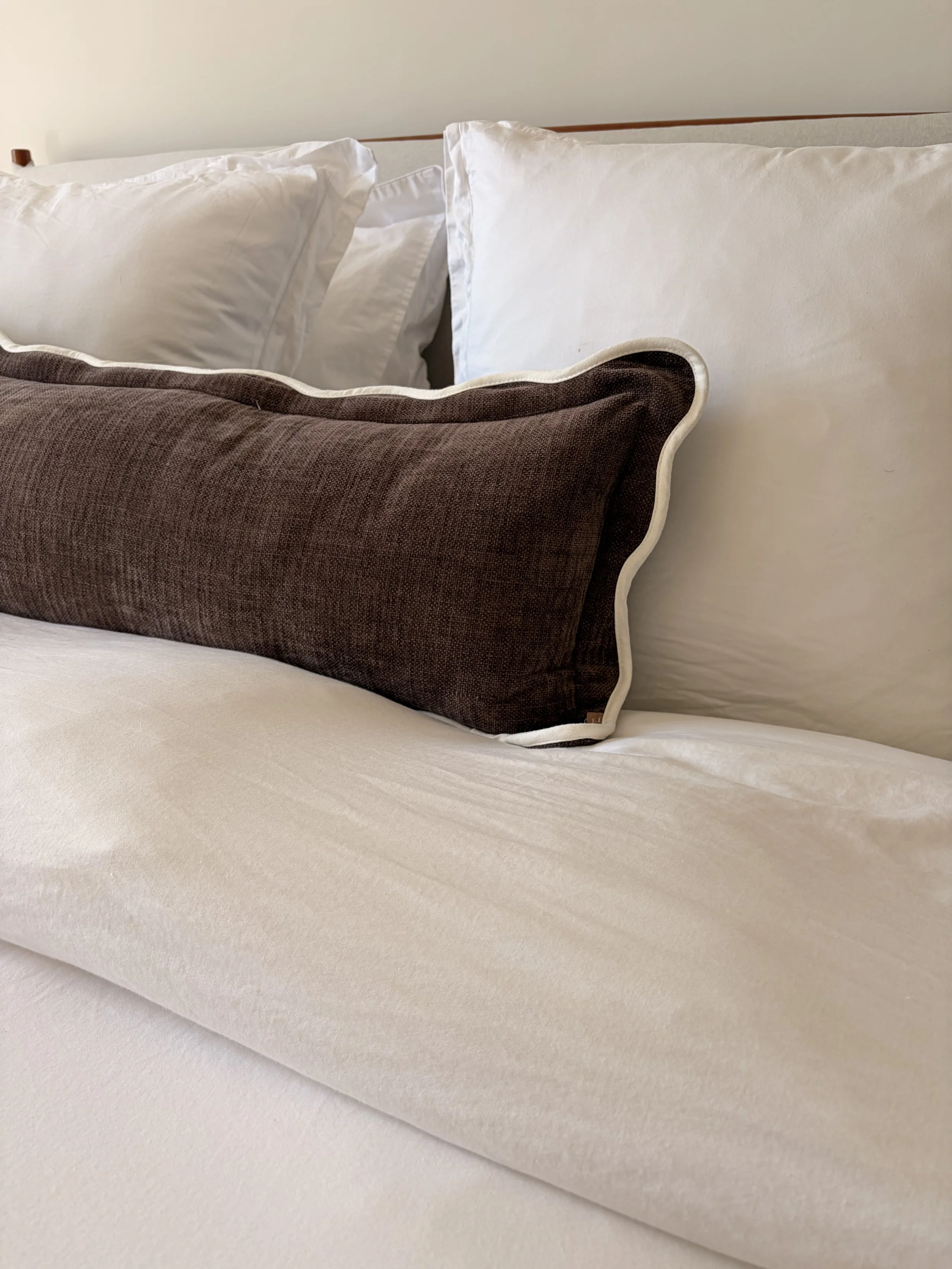 Close-up of a bed with white pillows and a dark brown decorative pillow on a white sheet