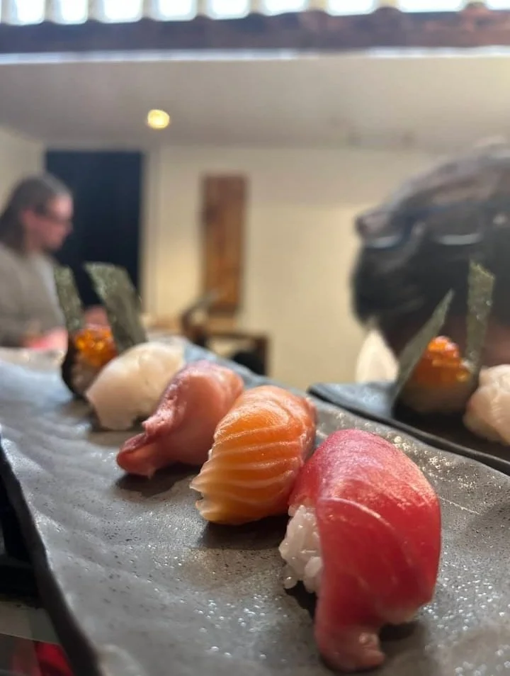 Close-up of a sushi platter with assorted sashimi and nigiri, with a person in the background in a restaurant setting.