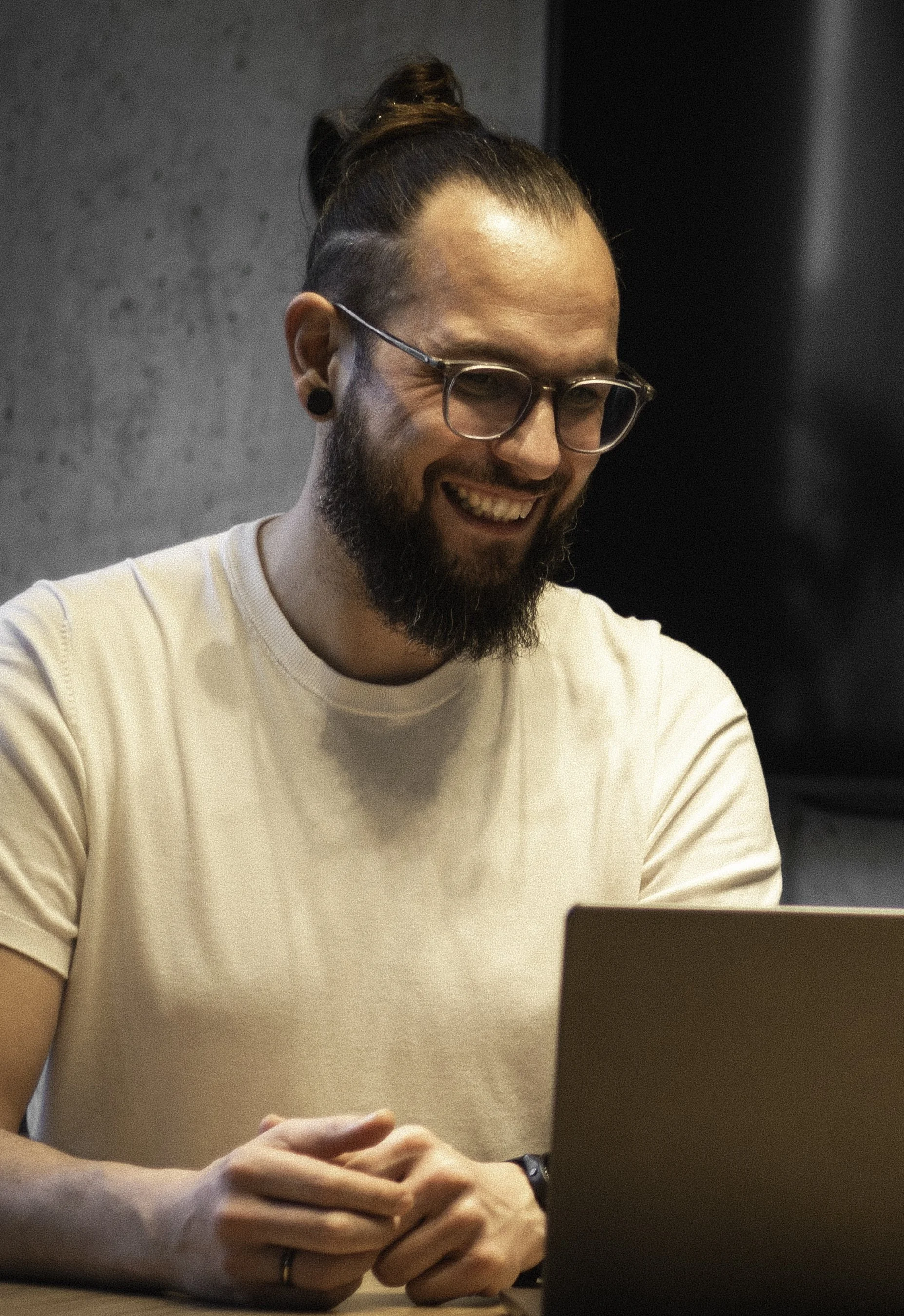 Ein lächelnder Mann mit Brille und Bart sitzt vor einem Laptop. Euer Ansprechpartner Karsten Hellinger Botenstoffe Consulting Healthcare Cybersecurity.