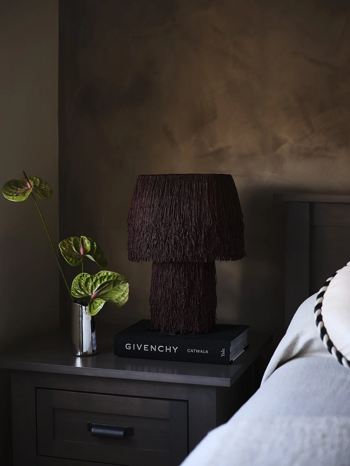 Gramercy Park primary bedroom detail — dark fringe table lamp, Givenchy Catwalk book, anthurium stem in chrome vase, limewash wall. New York luxury interiors. Vanessa Katzen Design. Photography by Frank Frances.