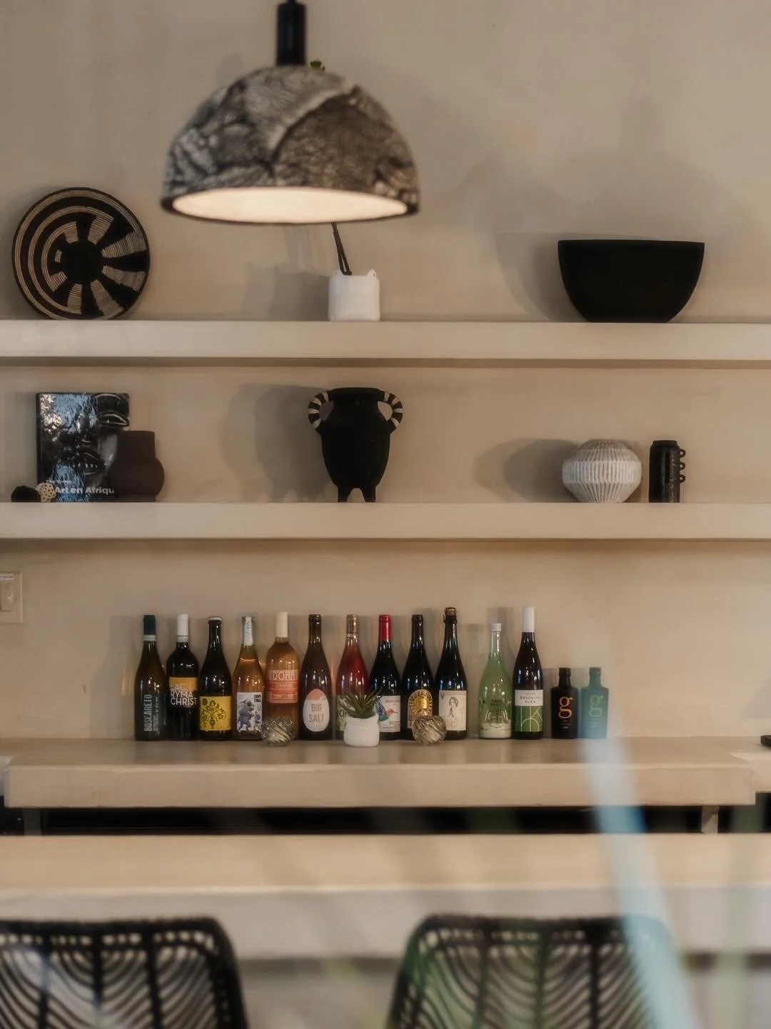 Wine bar display of decorative ceramic and glass vases, bottles of wine, and bowls arranged on white shelves in a modern interior.