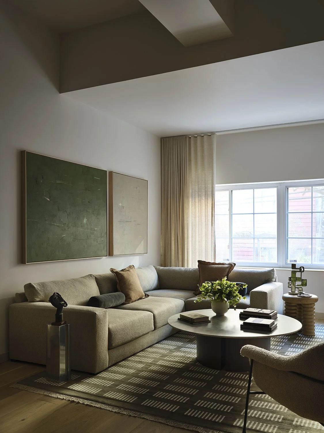 Park Slope carriage house living room — oversized abstract art, neutral boucle sectional, round concrete coffee table, geometric wool rug, linen drapery. Brooklyn luxury interior design. Vanessa Katzen Design. Photography by Frank Frances.