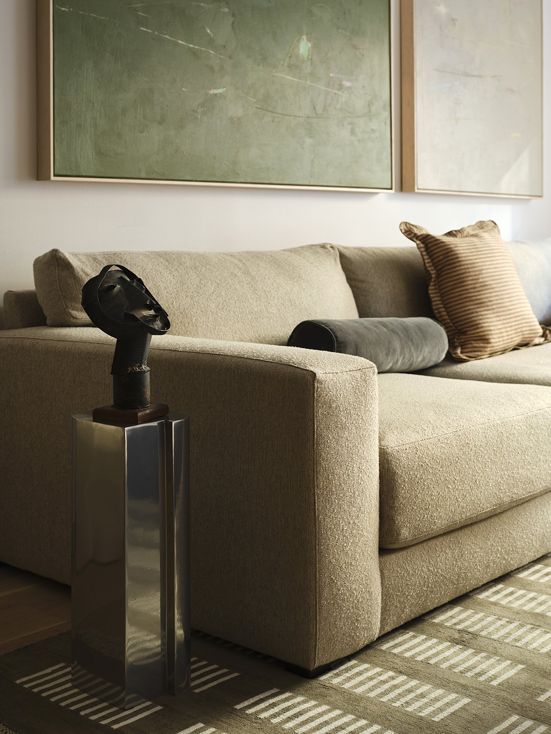 Modern living room with beige sofa, striped pillow, abstract paintings, and a unique black lamp on a metallic stand.