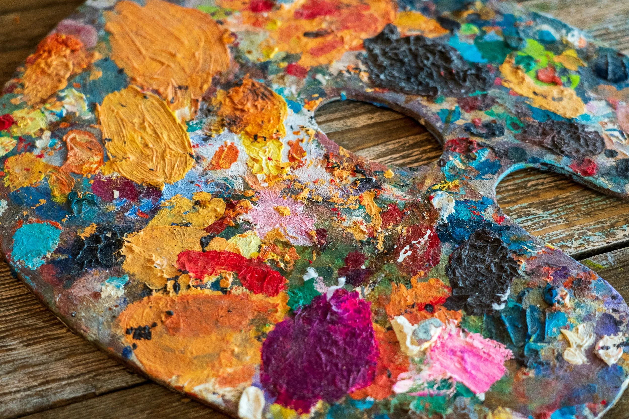 A CASA workshops de pintura e arte no Barreiro. Paleta de pintura suja com muitas cores vivas sobre uma superfície de madeira.