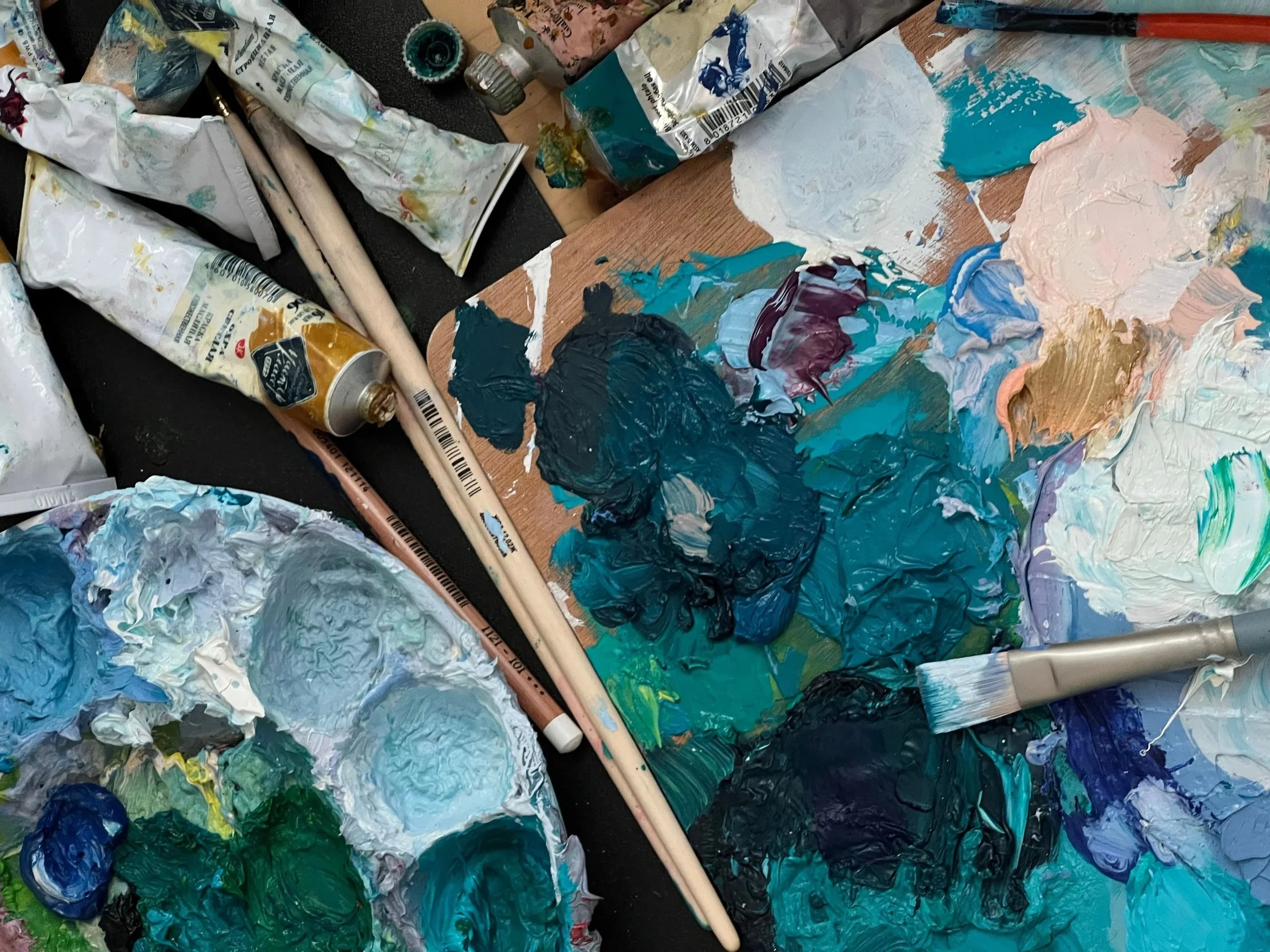 A CASA workshops de pintura e arte no Barreiro. Pincéis, tubos de tinta e pedaços de tinta espalhados em uma superfície, usados para pintura artística