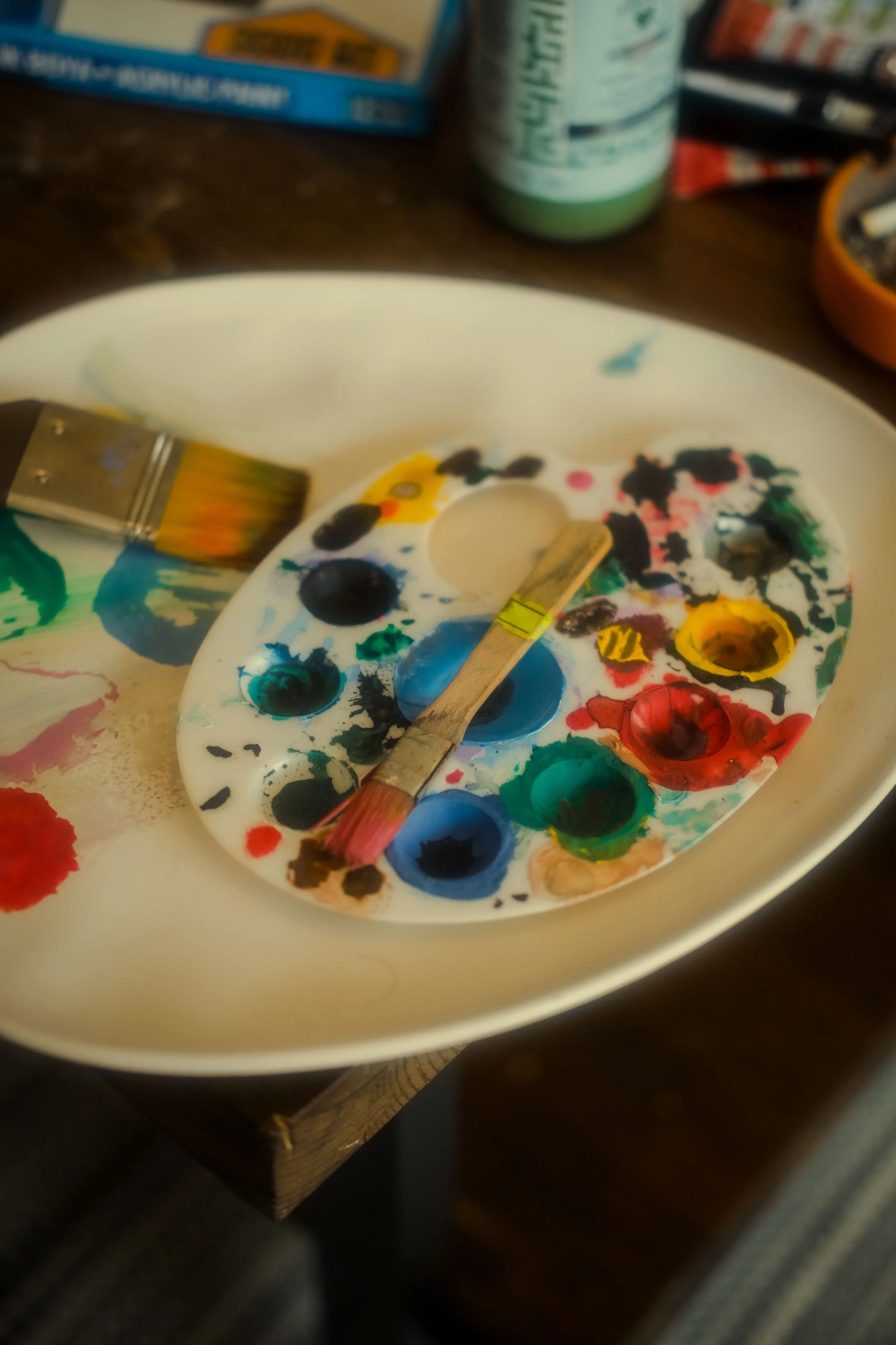 A CASA workshops de pintura e arte no Barreiro. Paleta de pintura com várias cores, duas pinceladas de tinta e outros materiais de arte em uma superfície de mesa.