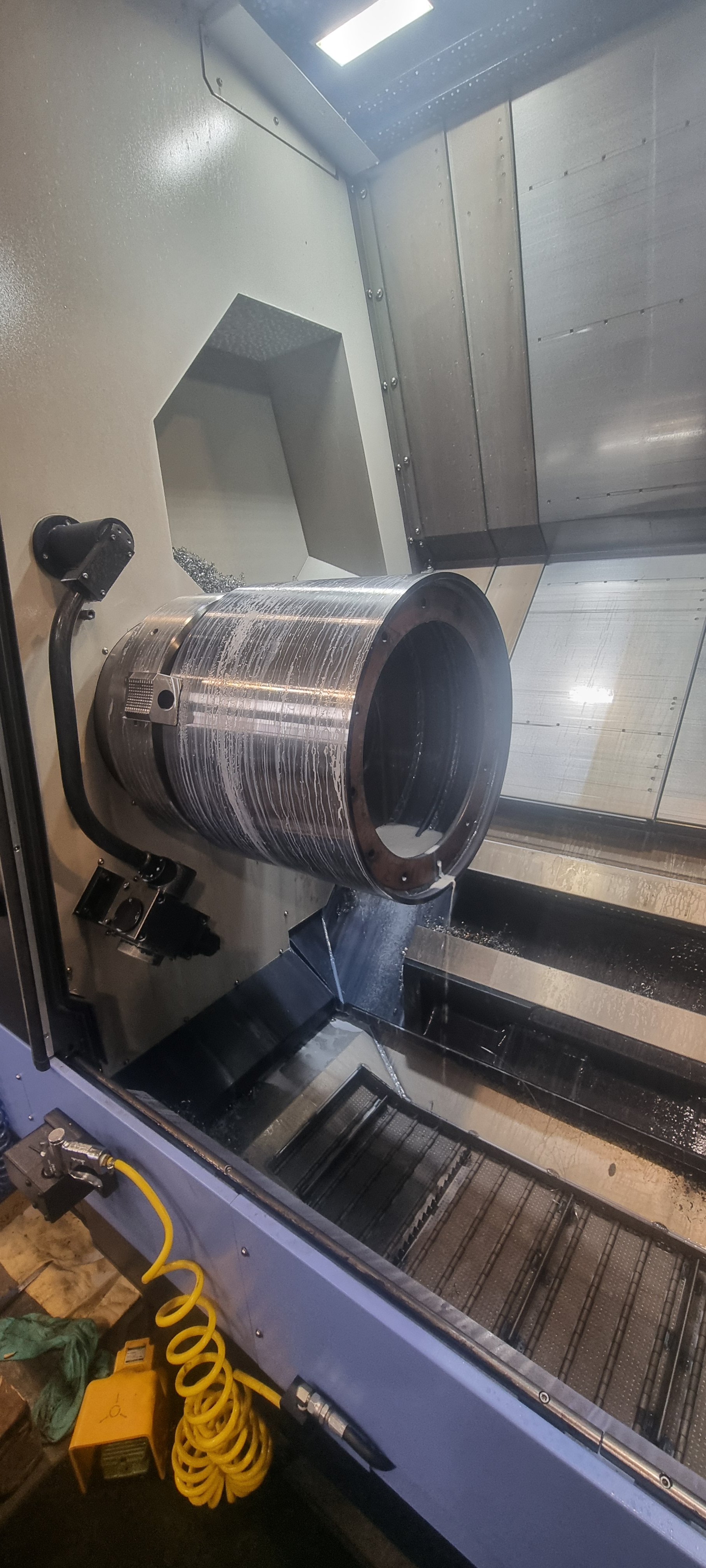 A CNC machine in operation with a metallic workpiece inside, water coolant being applied during machining.
