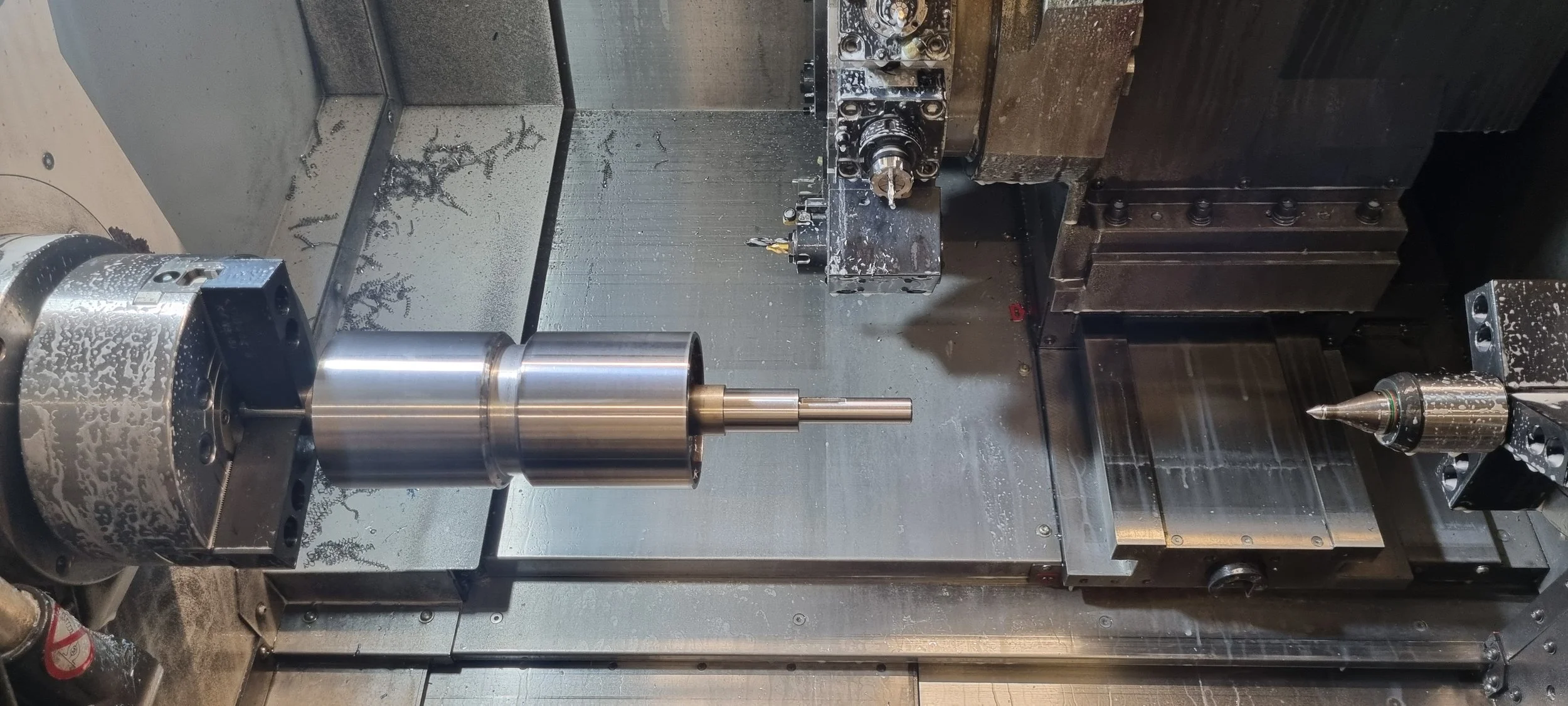 Close-up of a CNC machine with a metal workpiece and cutting tool, metal shavings scattered on the work surface.