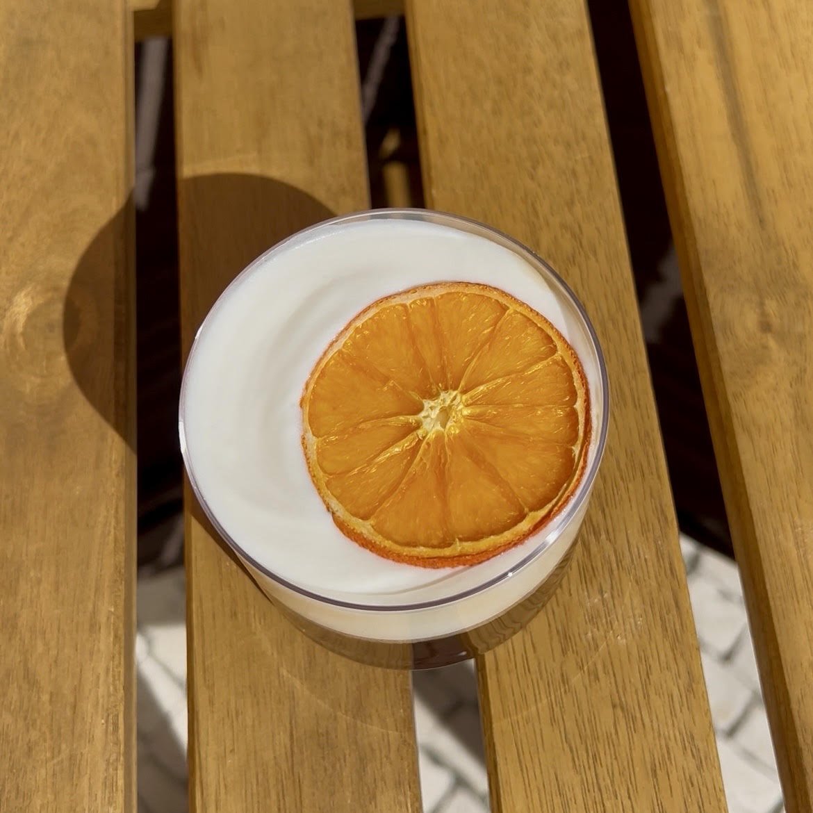 Copo com bebida branca, decorado com uma fatia de laranja seca por cima, colocado sobre uma mesa de madeira.