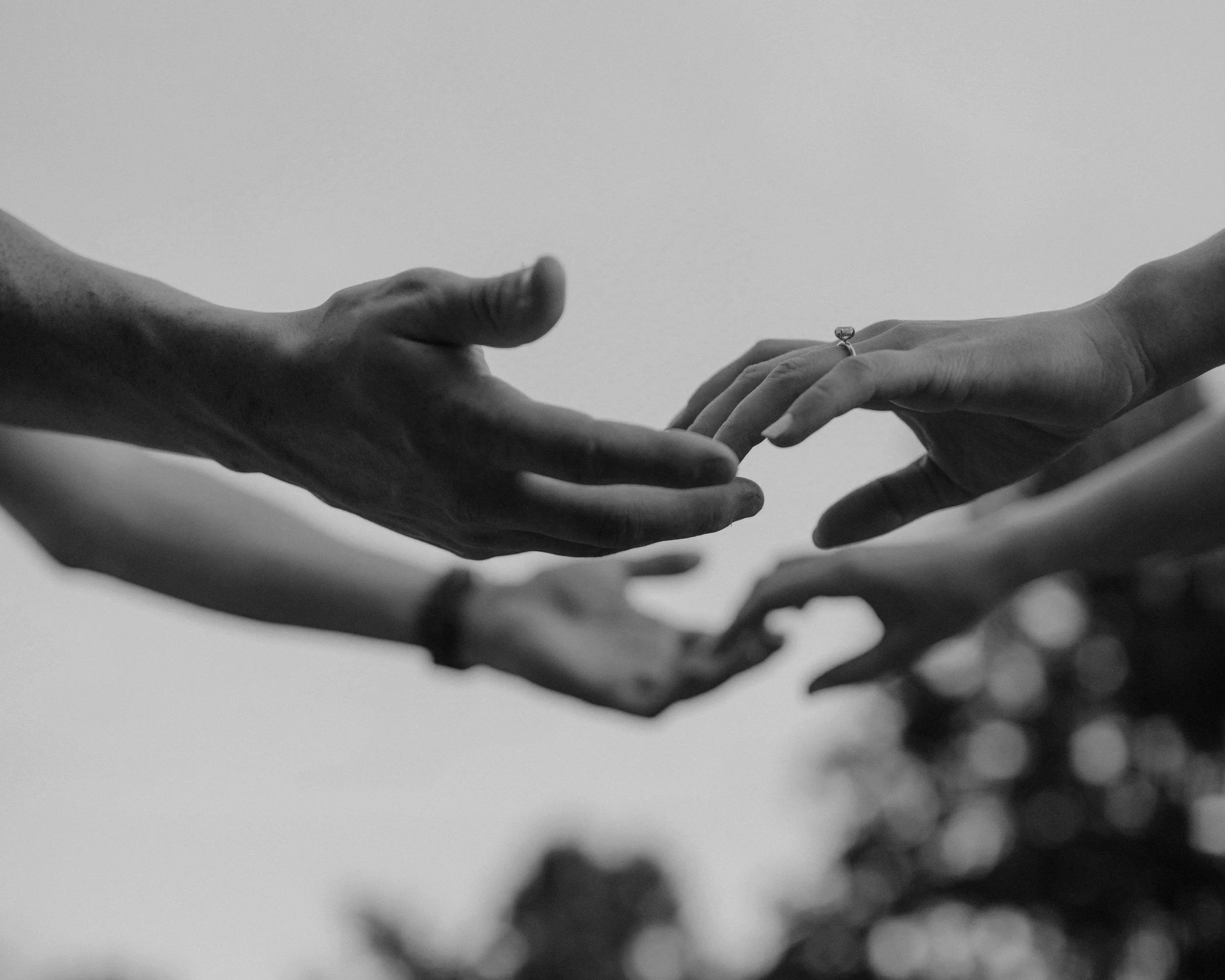 Black and white close-up of hands reaching toward each other, symbolising emotional connection, intimacy, and commitment in a healthy relationship.