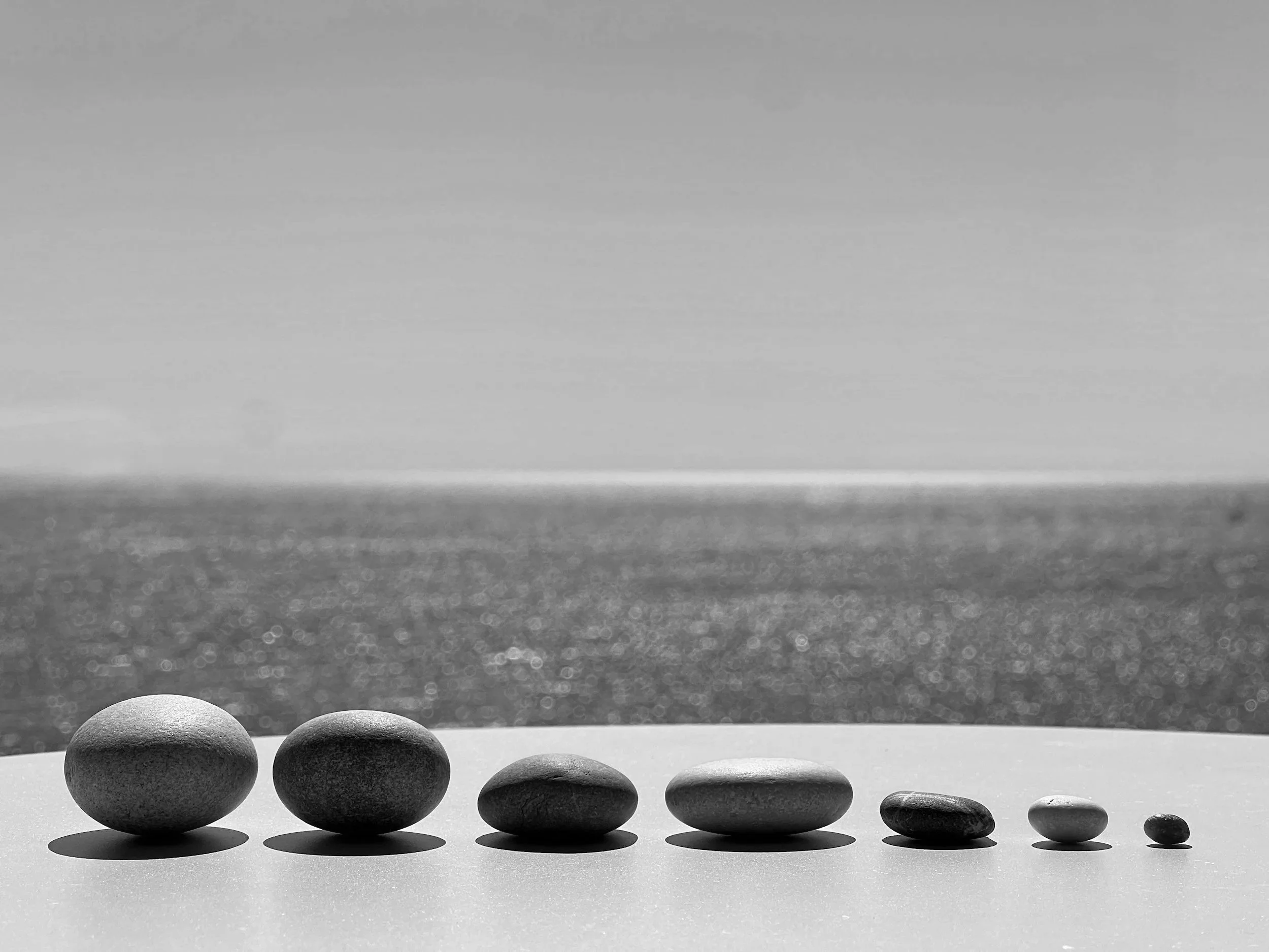 Black and white image of balanced stones lined up on a beach, symbolising emotional steadiness, grounding, and calm in relationships.
