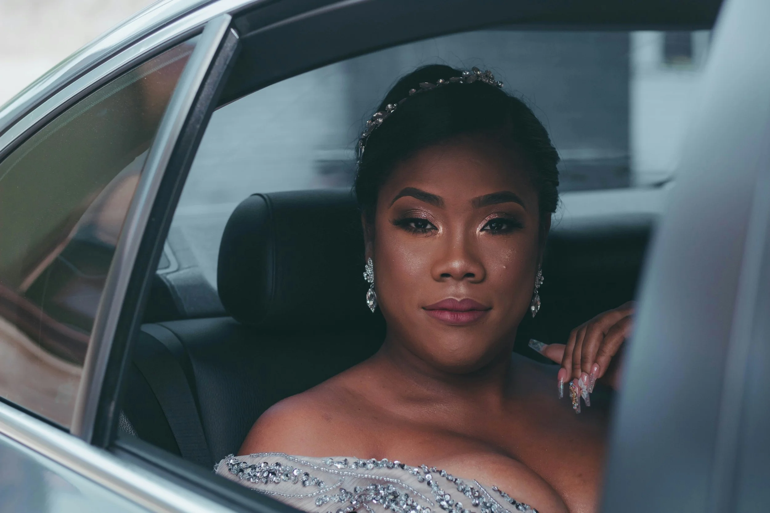 A woman with elegant makeup and jewelry sitting inside a car, seen through the window.