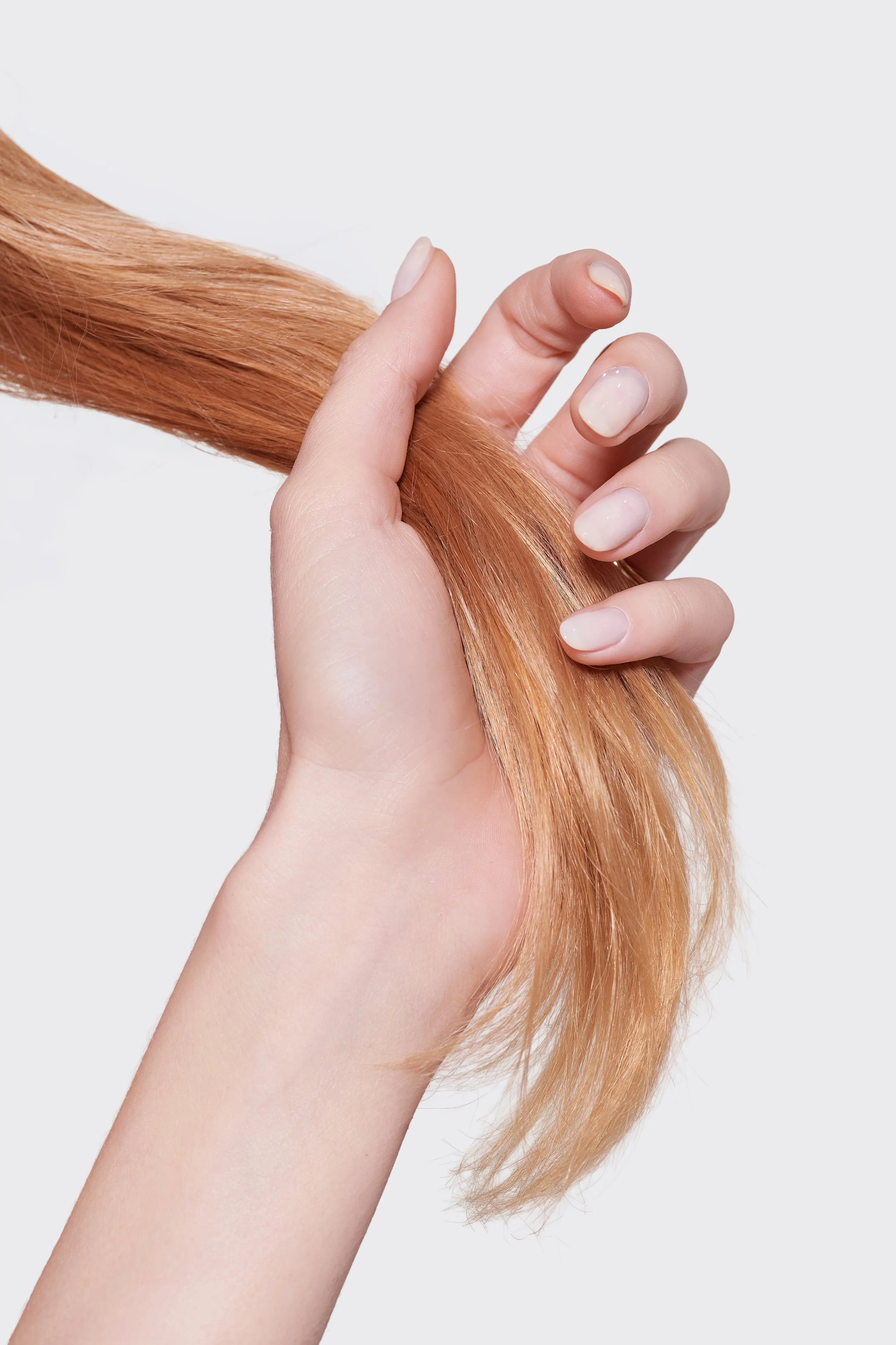 A hand holding a lock of long, straight, red hair against a plain white background.