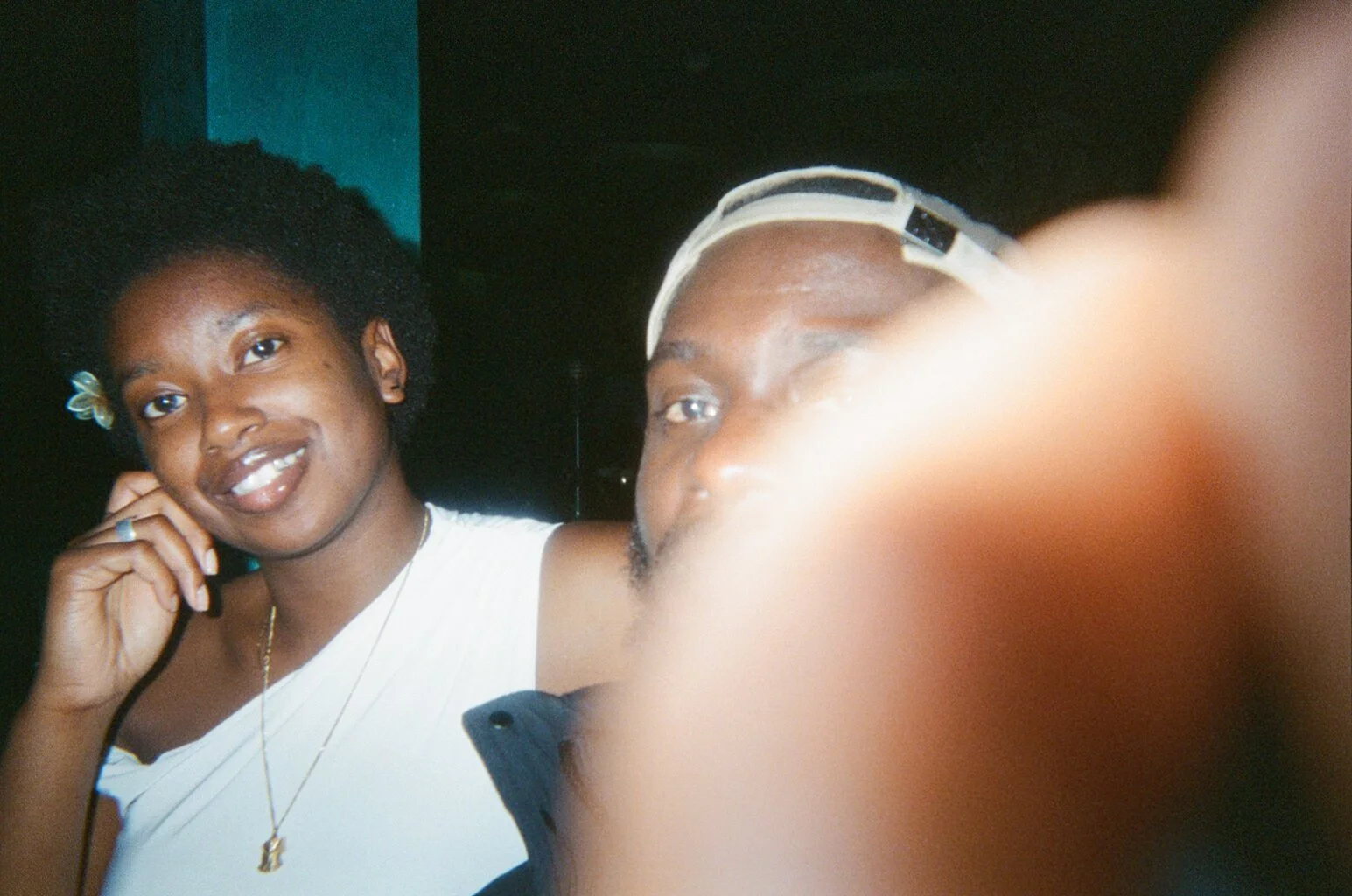 A woman smiling and posing for a photo with a man, who is partially obscured by the camera and appears to be wearing a cap.