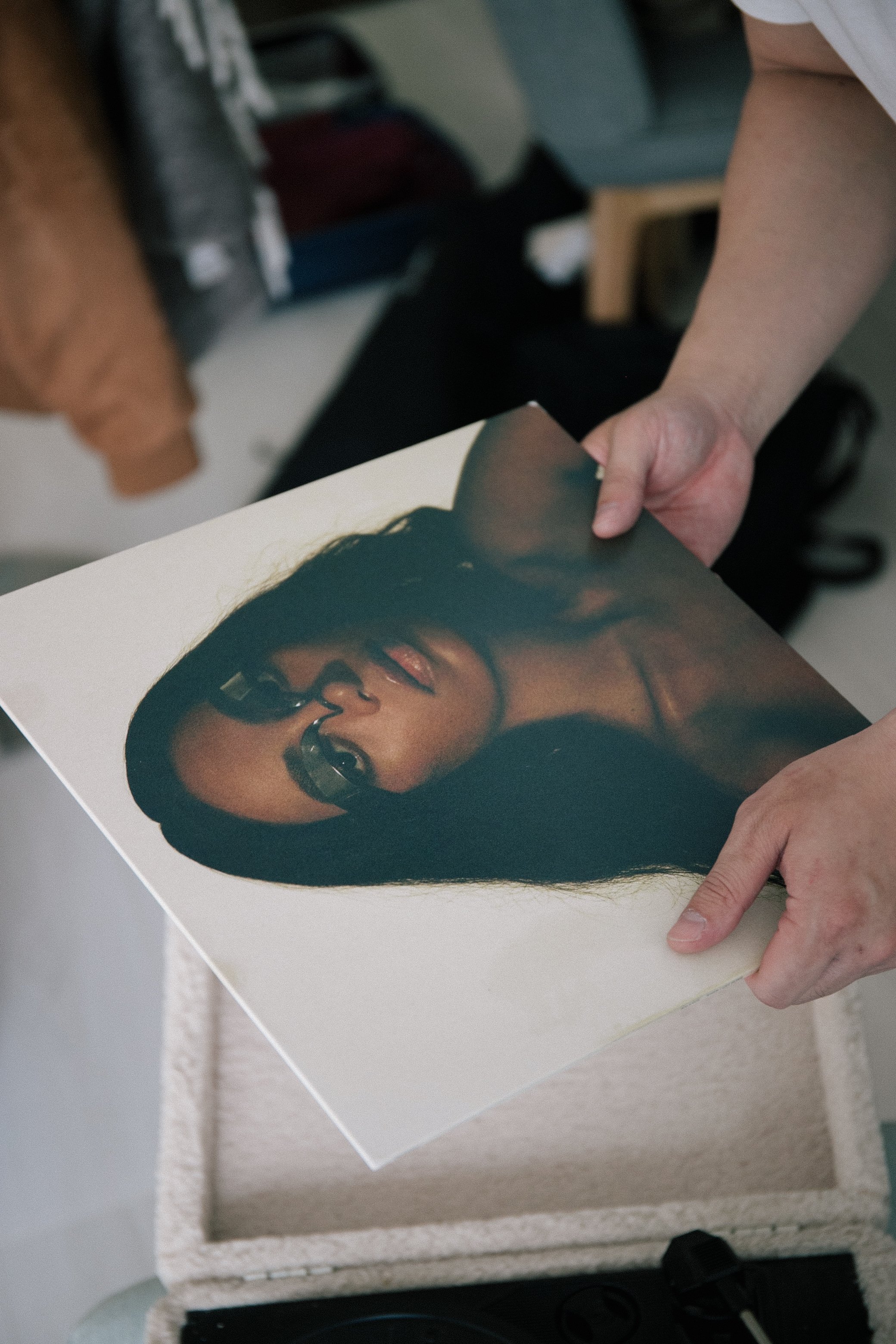 A person holding a Solange Vinyl (the cover shows a photo of a woman with dark hair and glasses) with part of their forearm and hand visible, near a textured white surface.