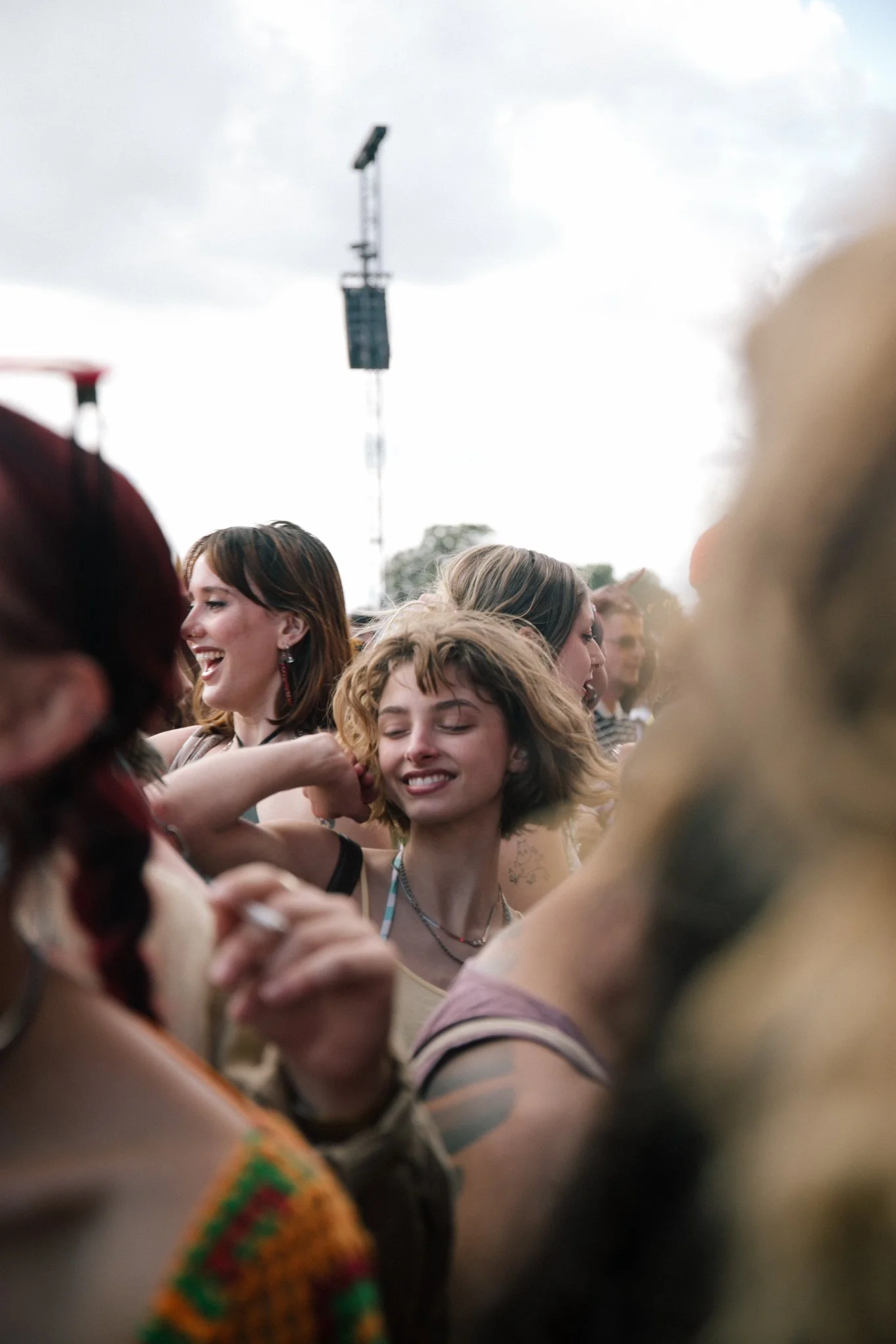 Group of young women smiling and dancing at an outdoor event on a cloudy day.