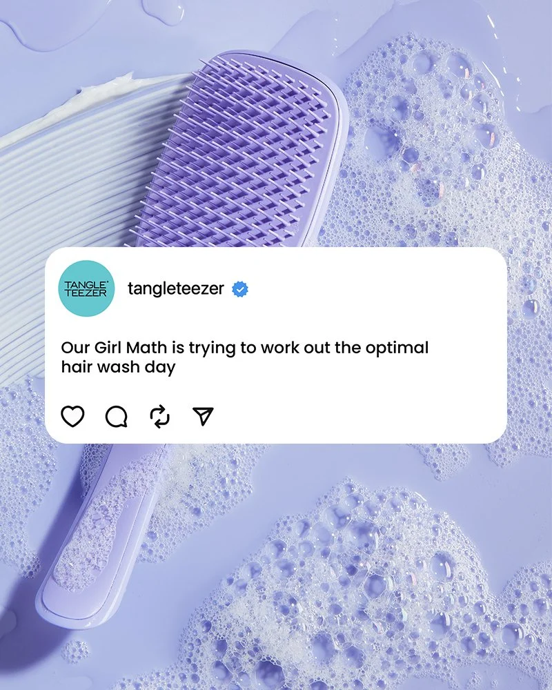 A purple hairbrush with a textured handle resting on a wet surface with bubbles, soap suds, and water.