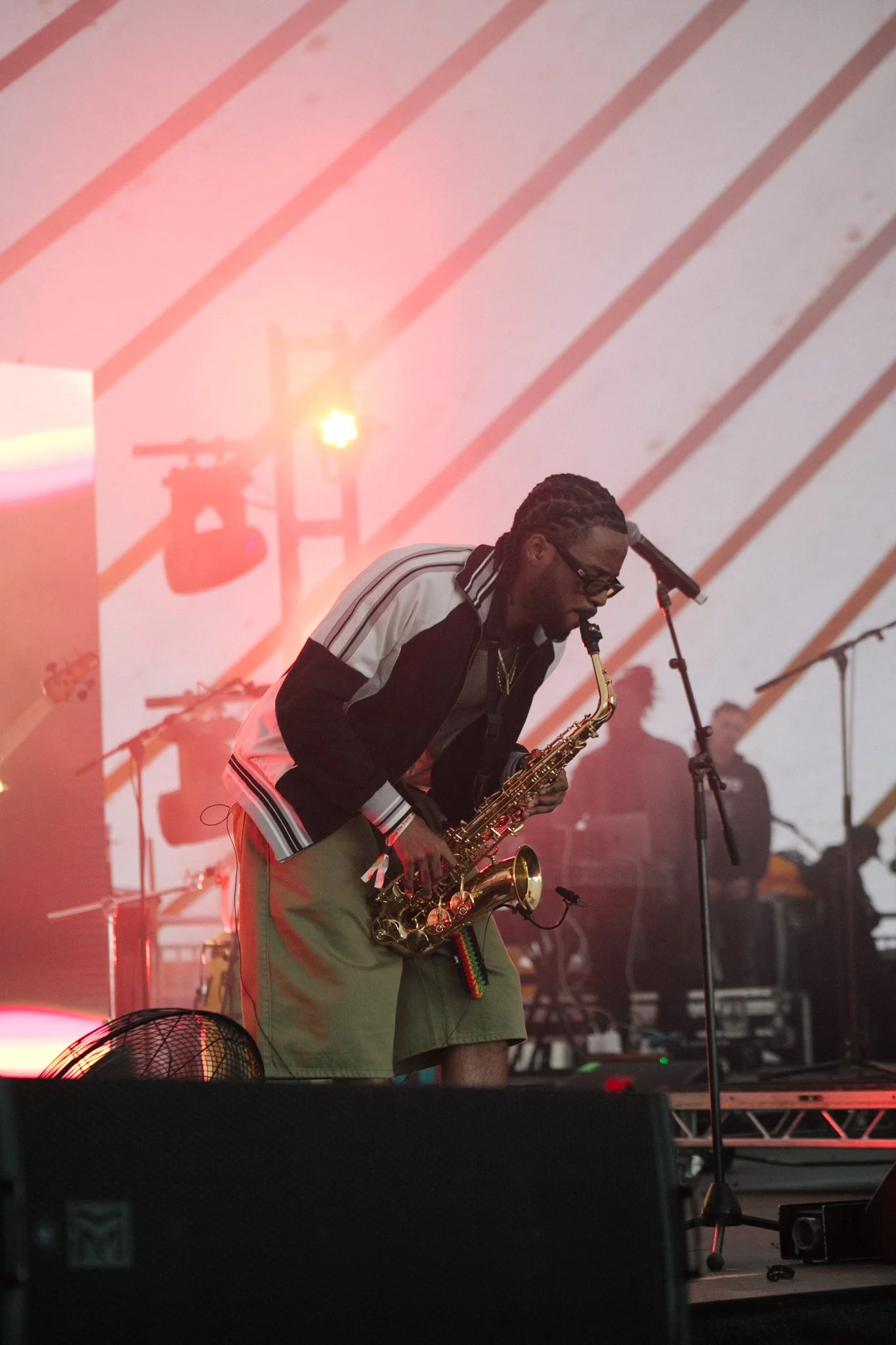Musician Venna playing a saxophone on stage with red and pink lighting and a background projection of cafe imagery.