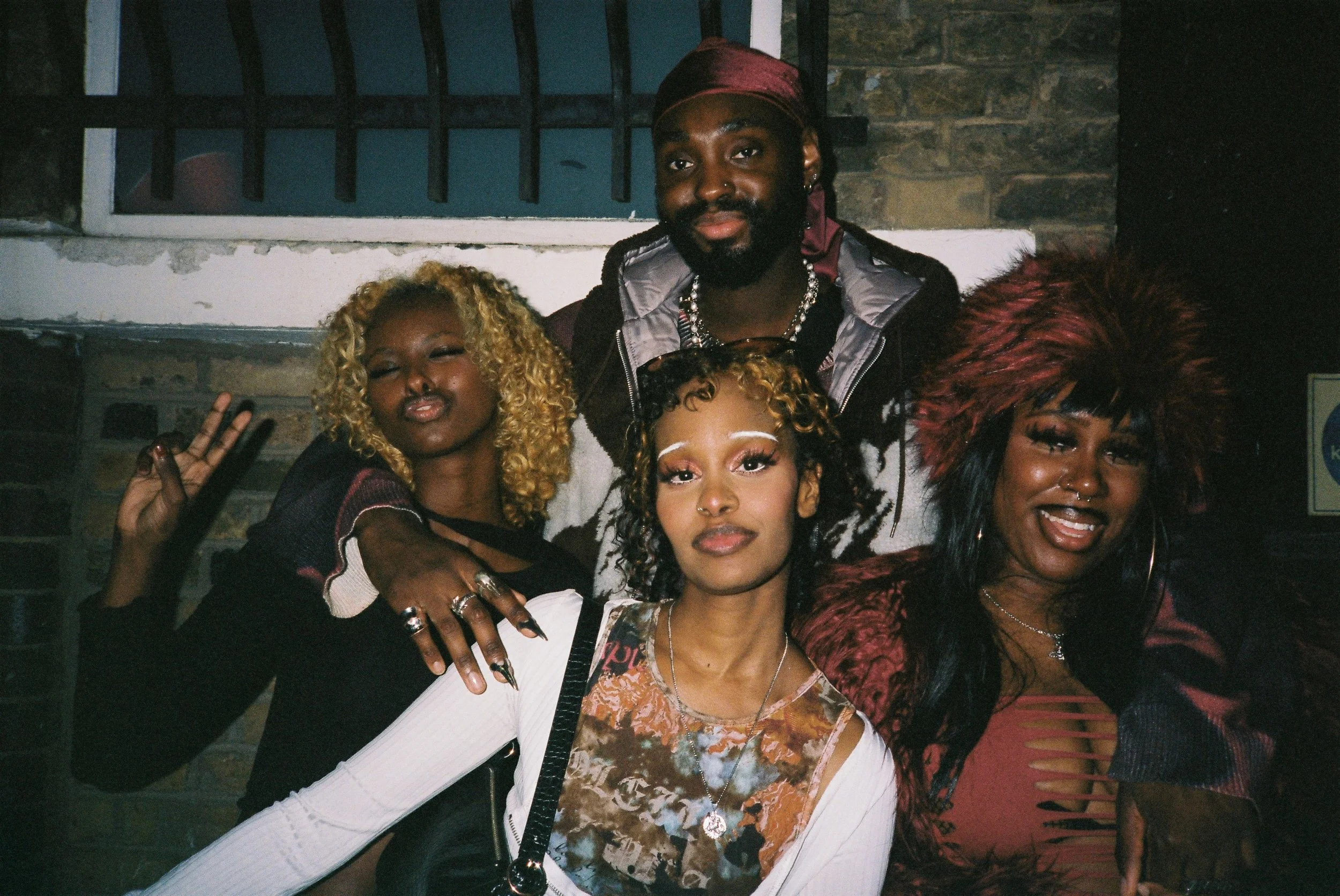 A group of friends gathered together, smiling and posing for a photo, with some showing hand gestures.