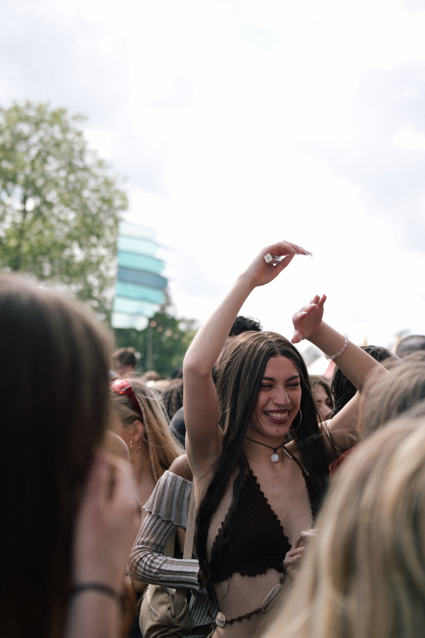 A young woman with long black hair, smiling and dancing at an outdoor event among a crowd of people.