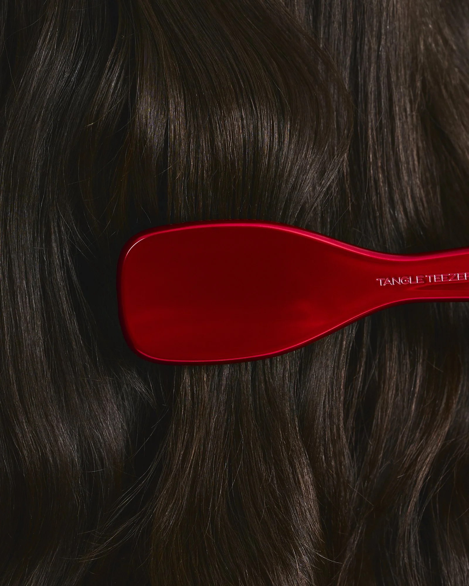 Close-up of dark brown hair with a red hairbrush