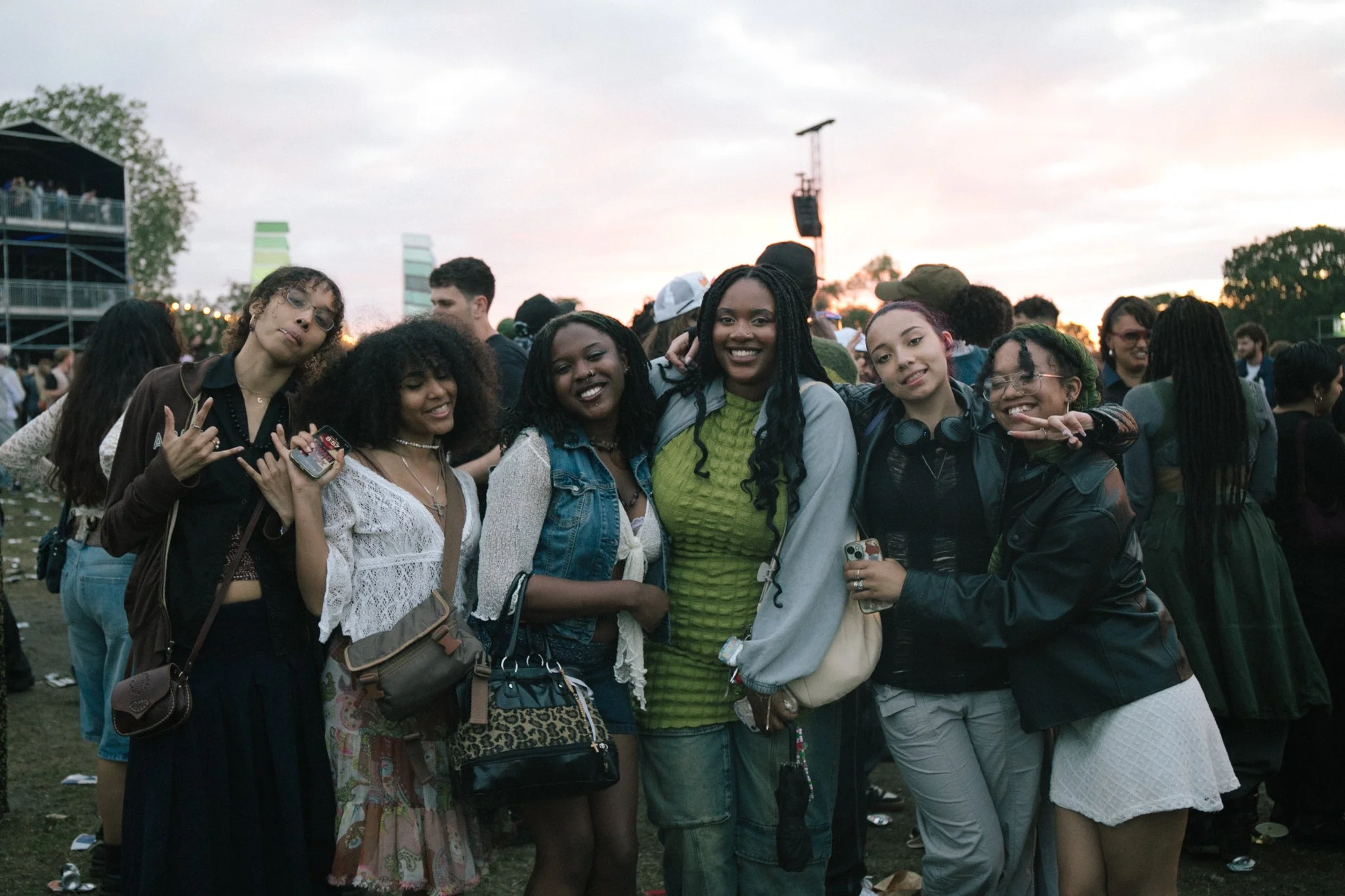 Group of young women at an outdoor concert or festival during sunset, smiling and posing for the camera.