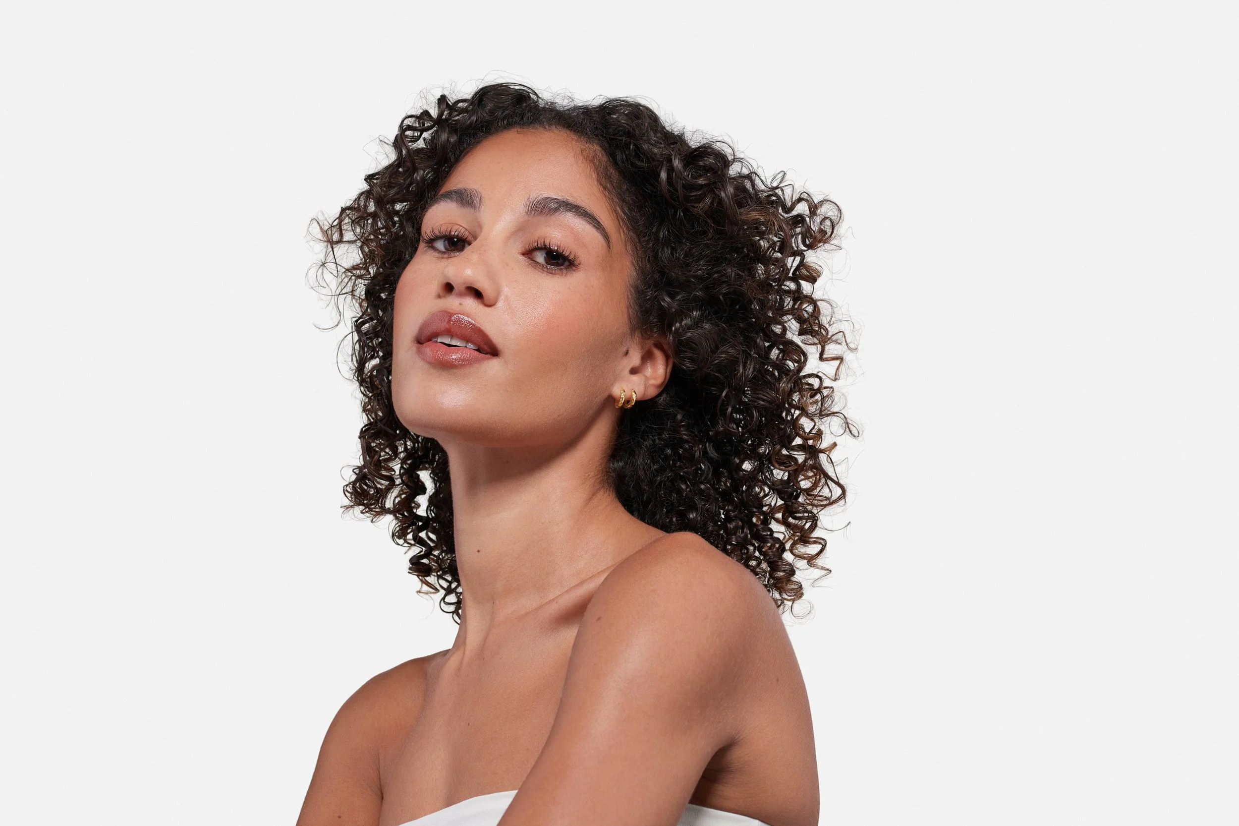 A woman with curly brown hair and medium skin tone looking at the camera against a plain white background.