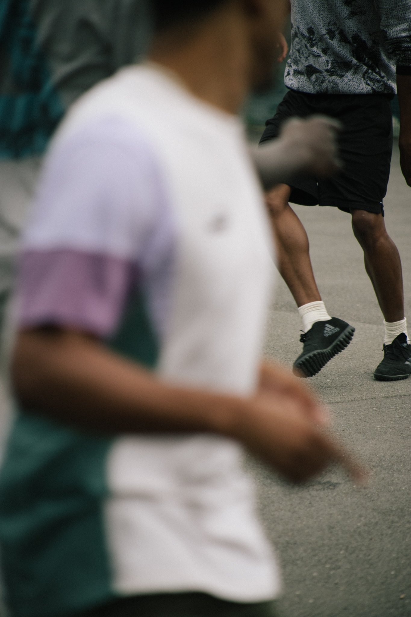 People stretching and exercising outdoors, with one person in a gray patterned shirt and black shorts. One figured is blurred in the foreground.