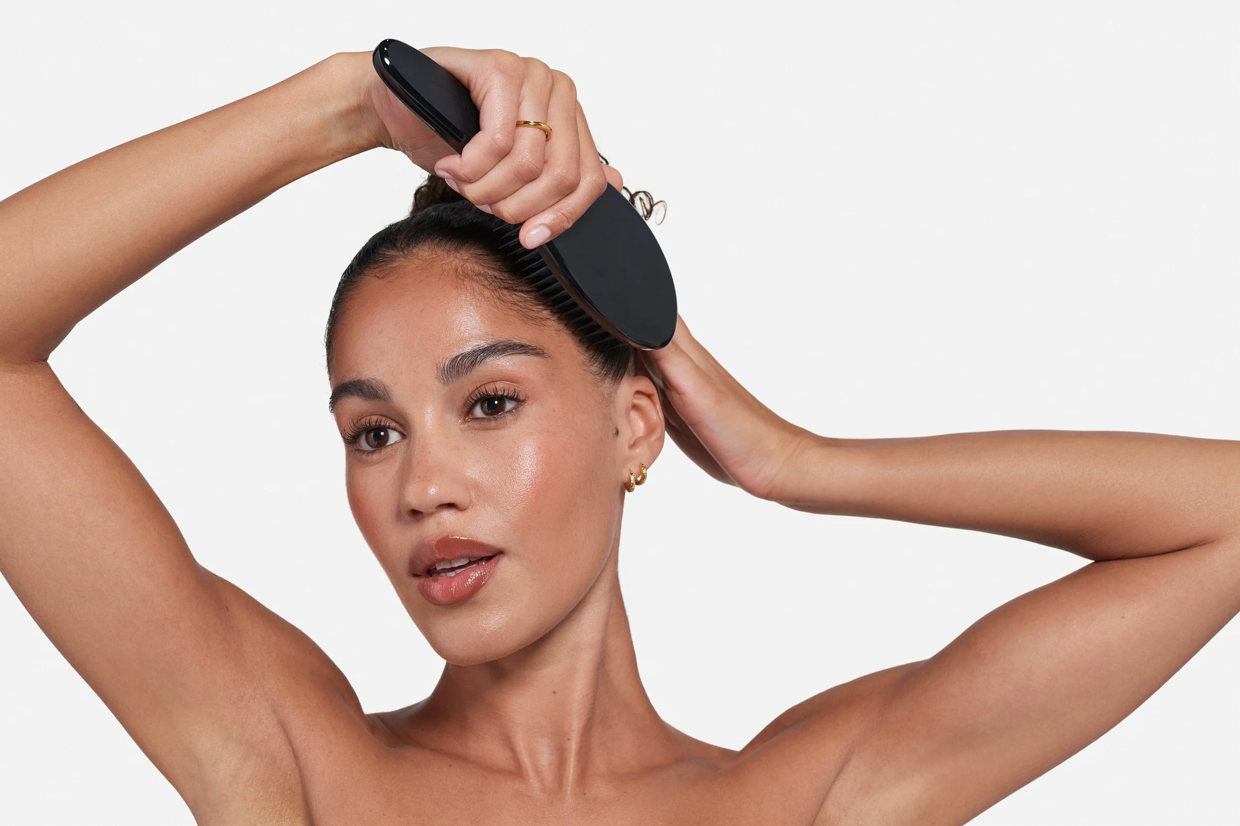 A woman with brown hair smoothing her hair with a black brush.