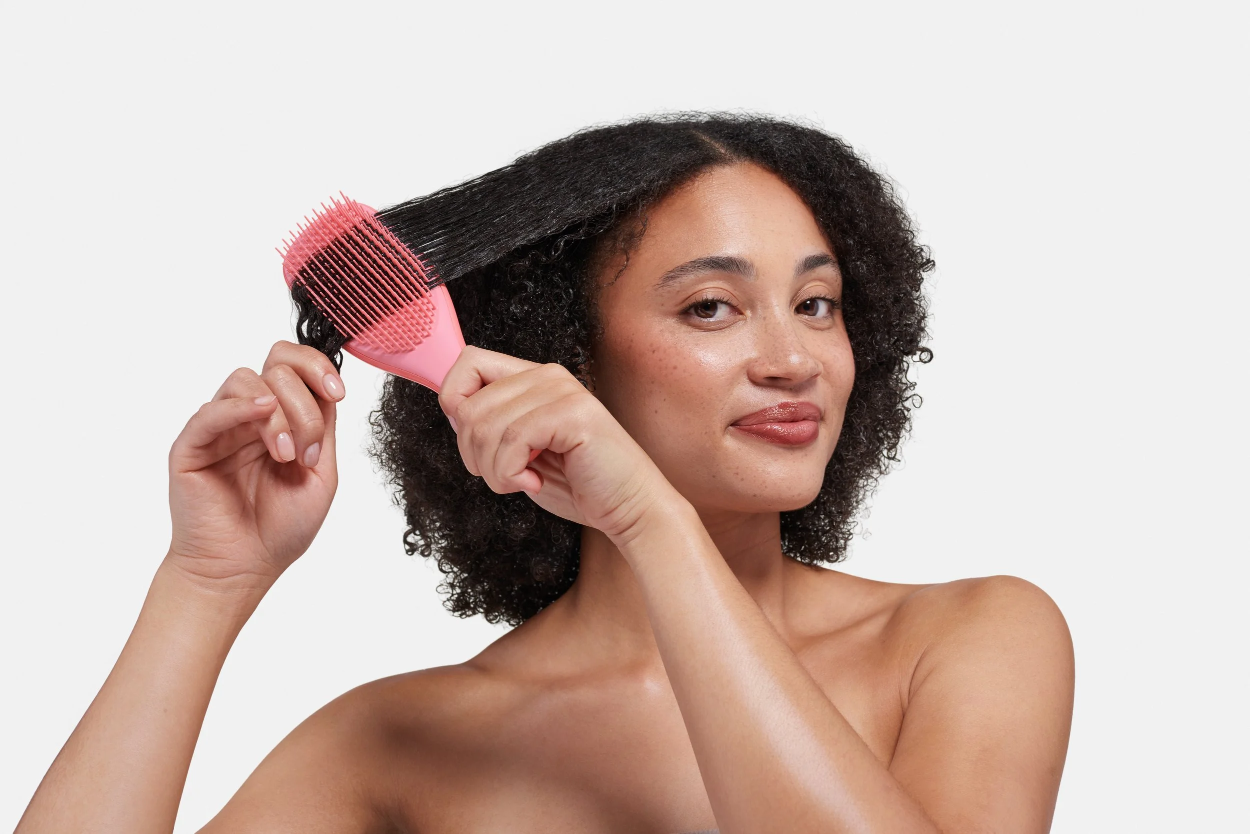 A woman with curly dark hair using a pink hairbrush to detangle her hair.