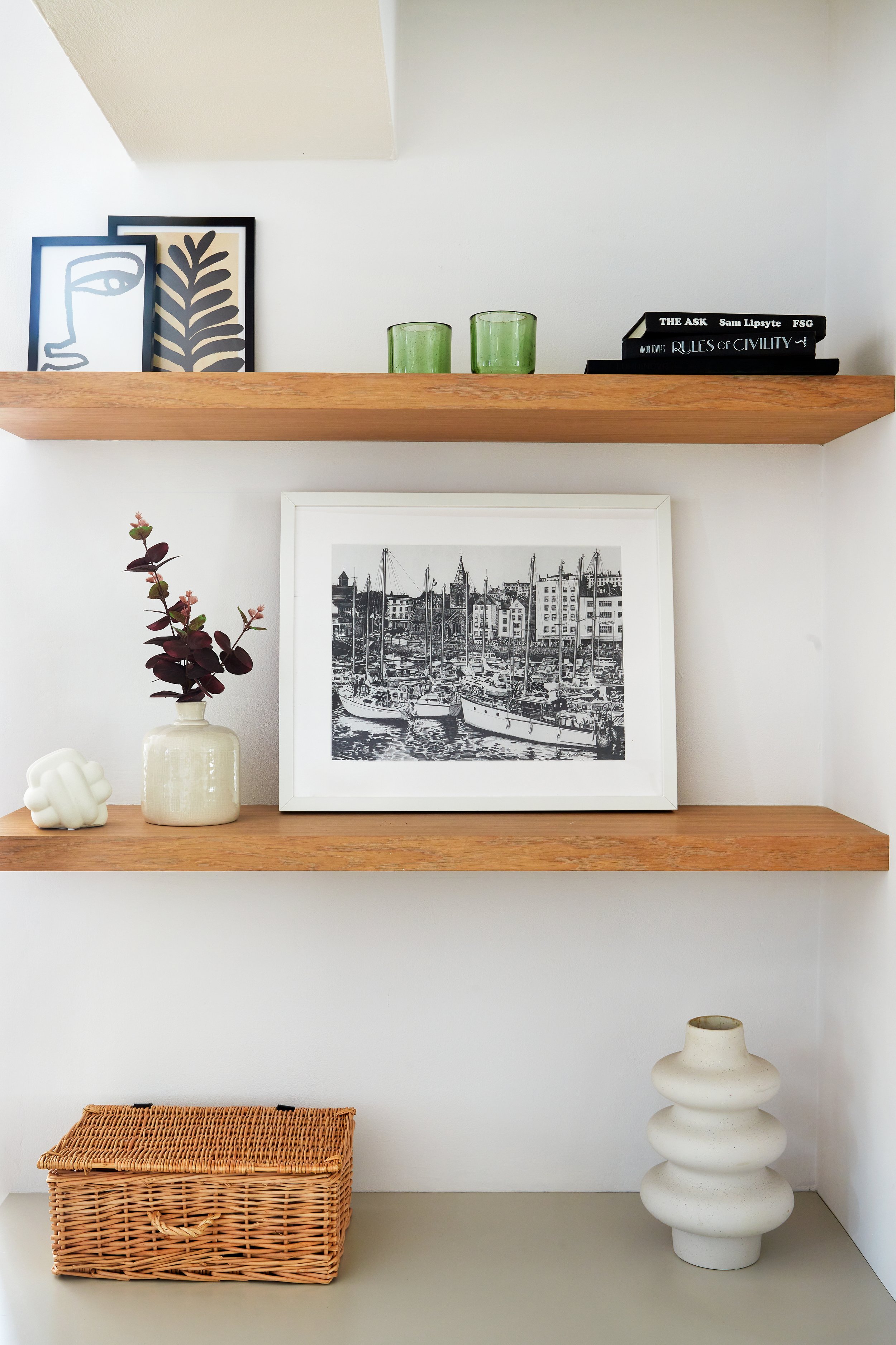 Decorative shelves with framed artwork, small vases, books, a green candle holder, a wicker basket, and a white ceramic vase.