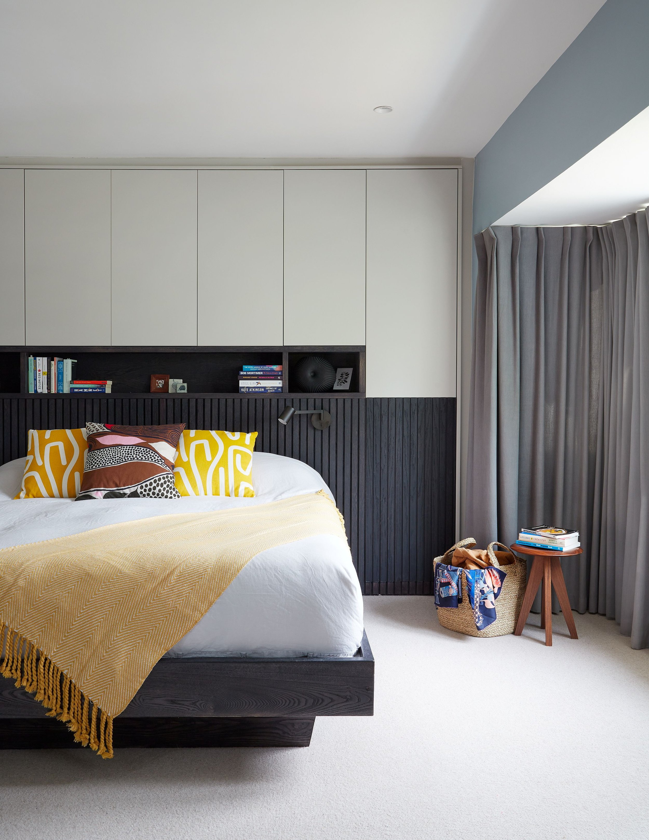 Modern bedroom with black and white color scheme, yellow throw blanket, patterned pillows, books, and a small side table with additional books and a bag near the window.