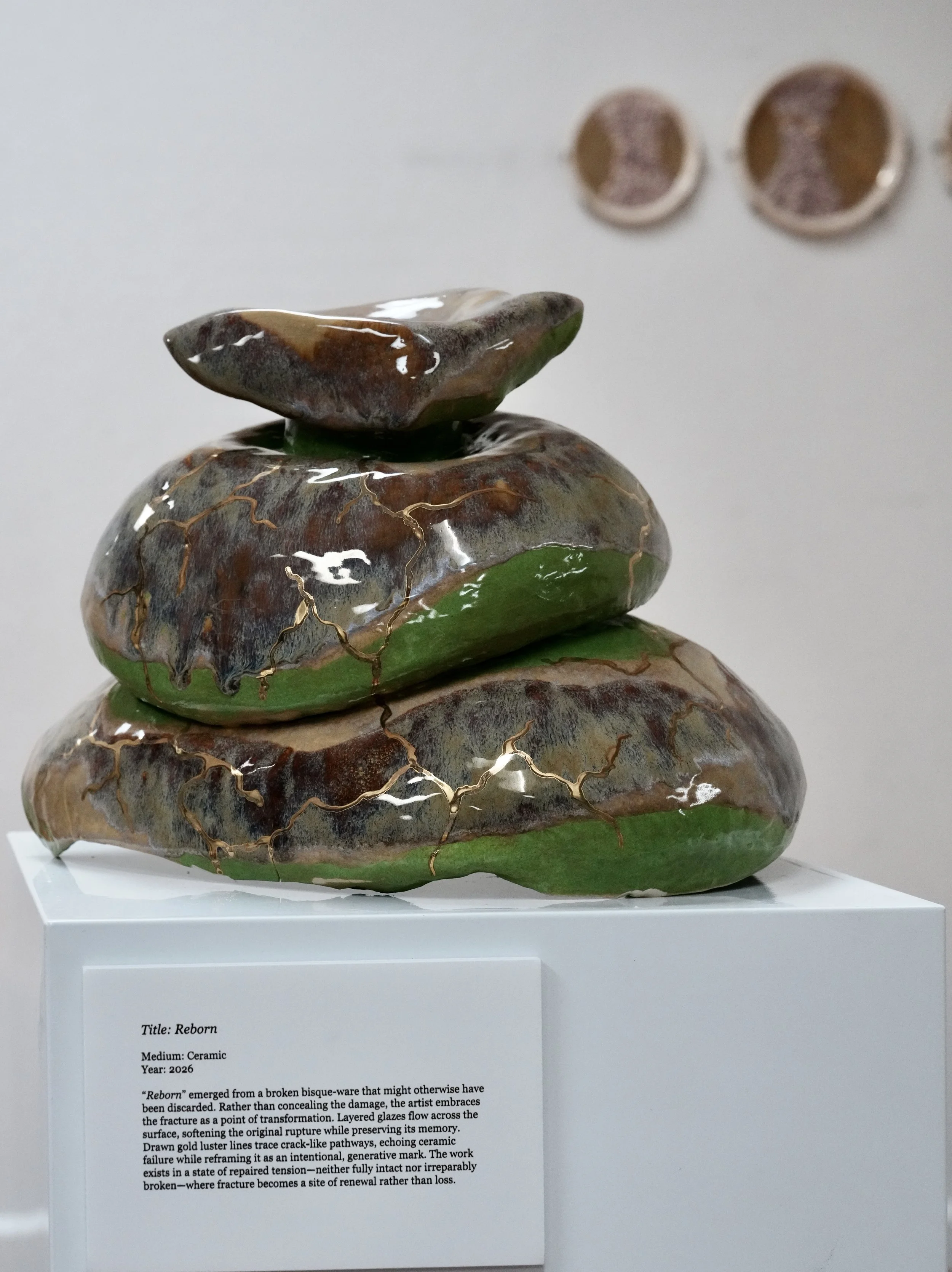 Ceramic sculpture titled Reborn, 2026, featuring layered, cracked glaze resembling broken pottery, on display at an exhibition.
