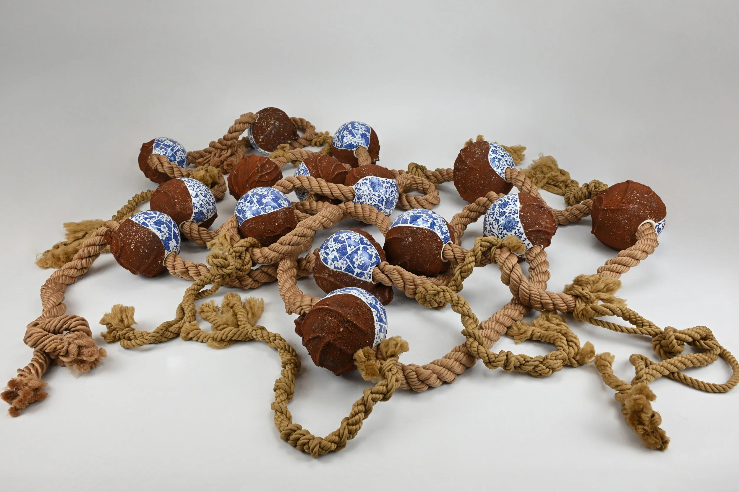 Collection of brown and blue patterned ceramic balls connected by tan braided ropes on a plain white background.