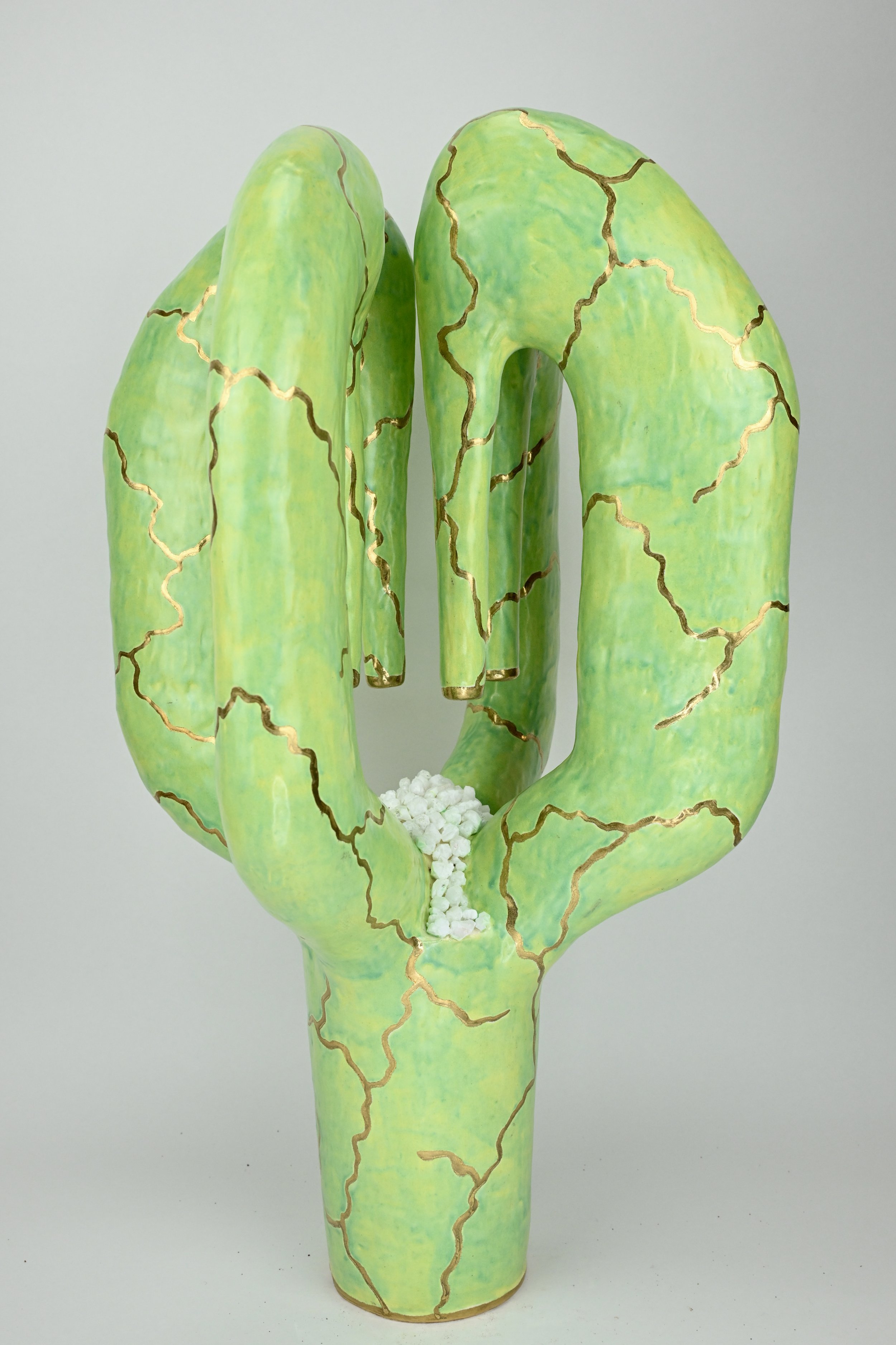 Art sculpture of a green cactus with gold cracks, holding white small objects at the base.