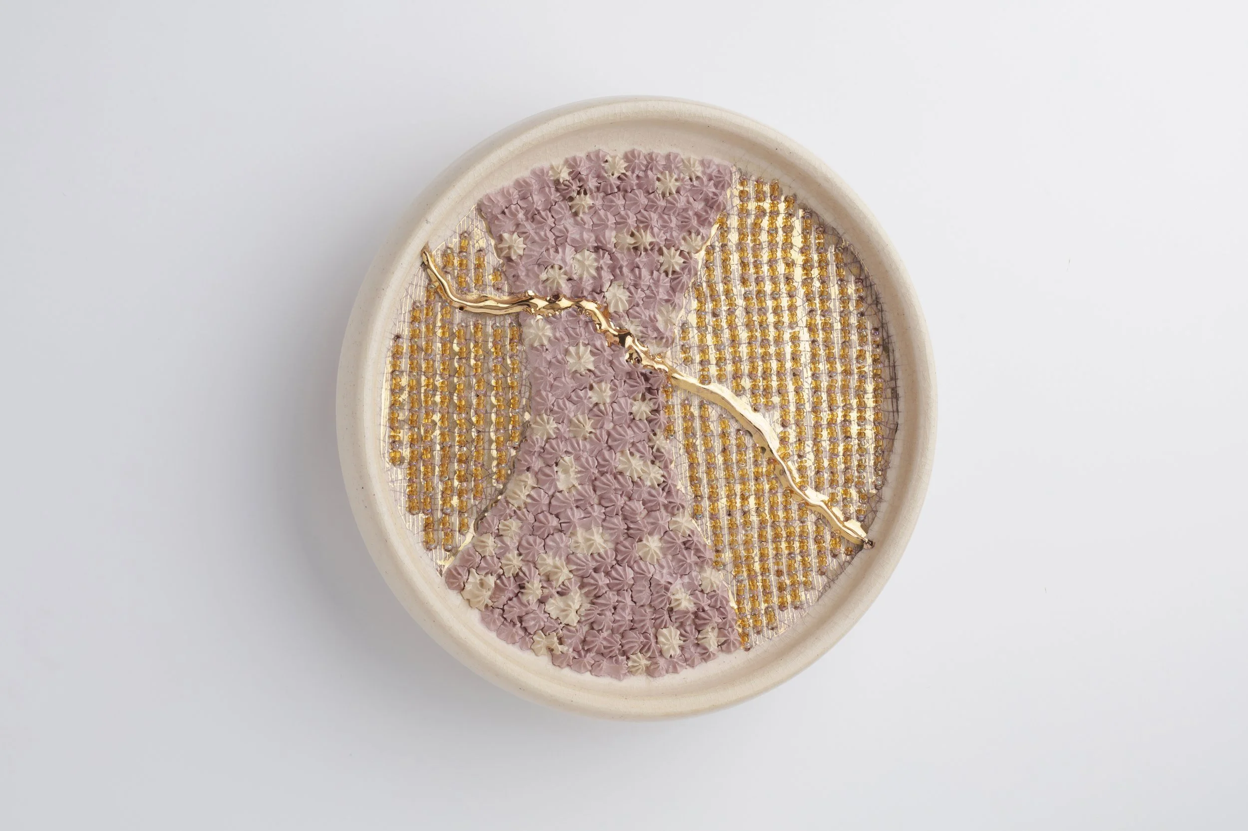 Decorative circular piece with a floral mosaic pattern inside a beige container, featuring pink, beige, and gold elements.