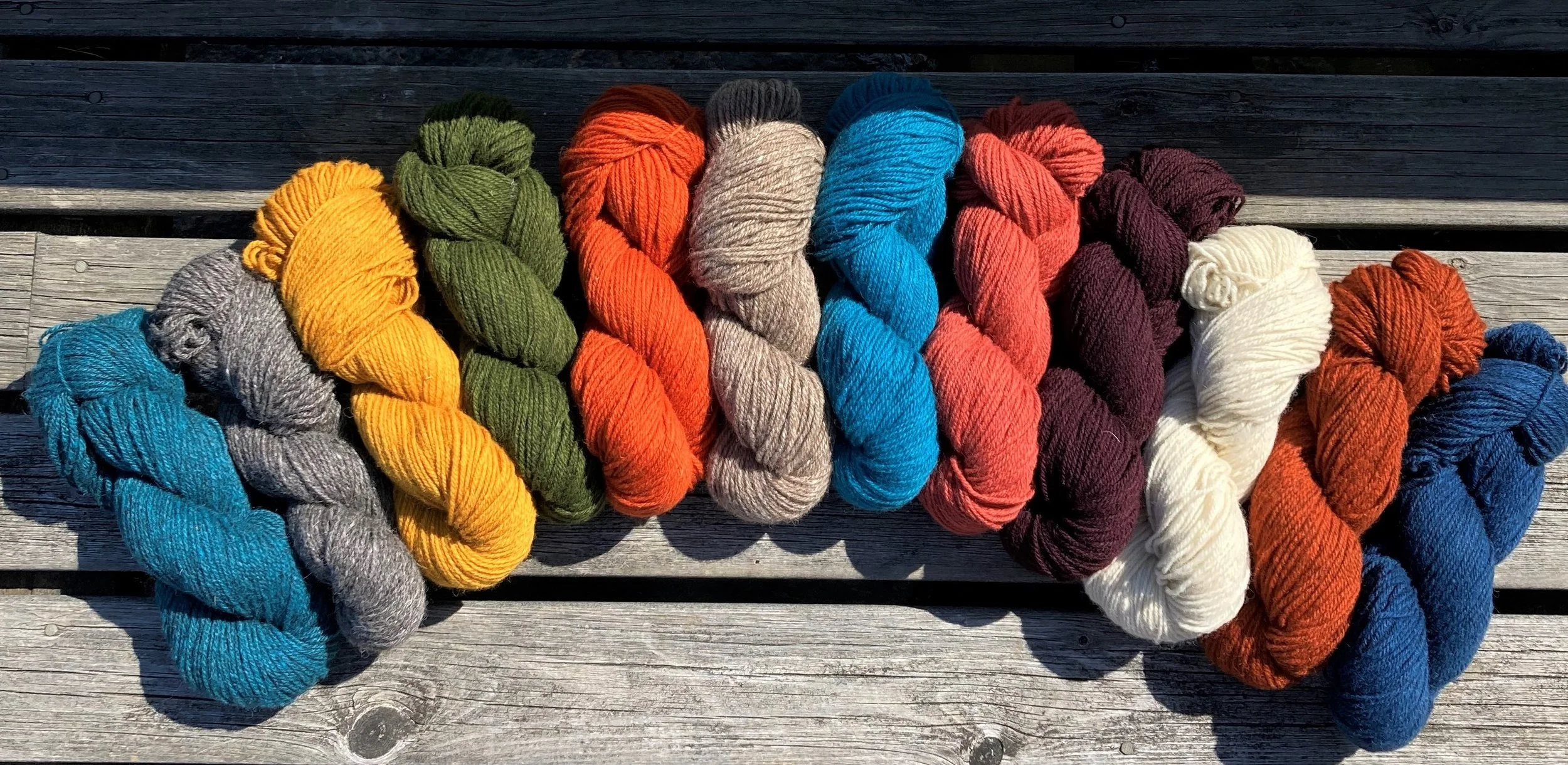 Erivärisiä lankakeriä aseteltuna riviin ulkona.