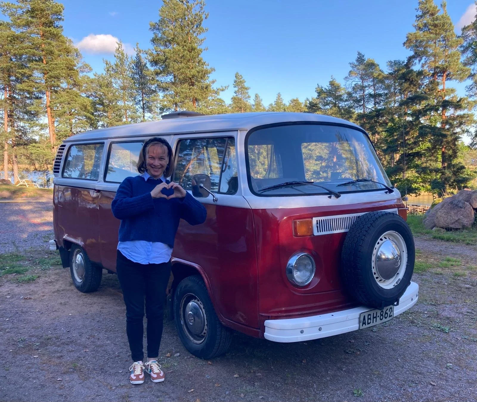 Nainen seisoo punaisen vanhan Wolksvagen-pakettiauton edessä