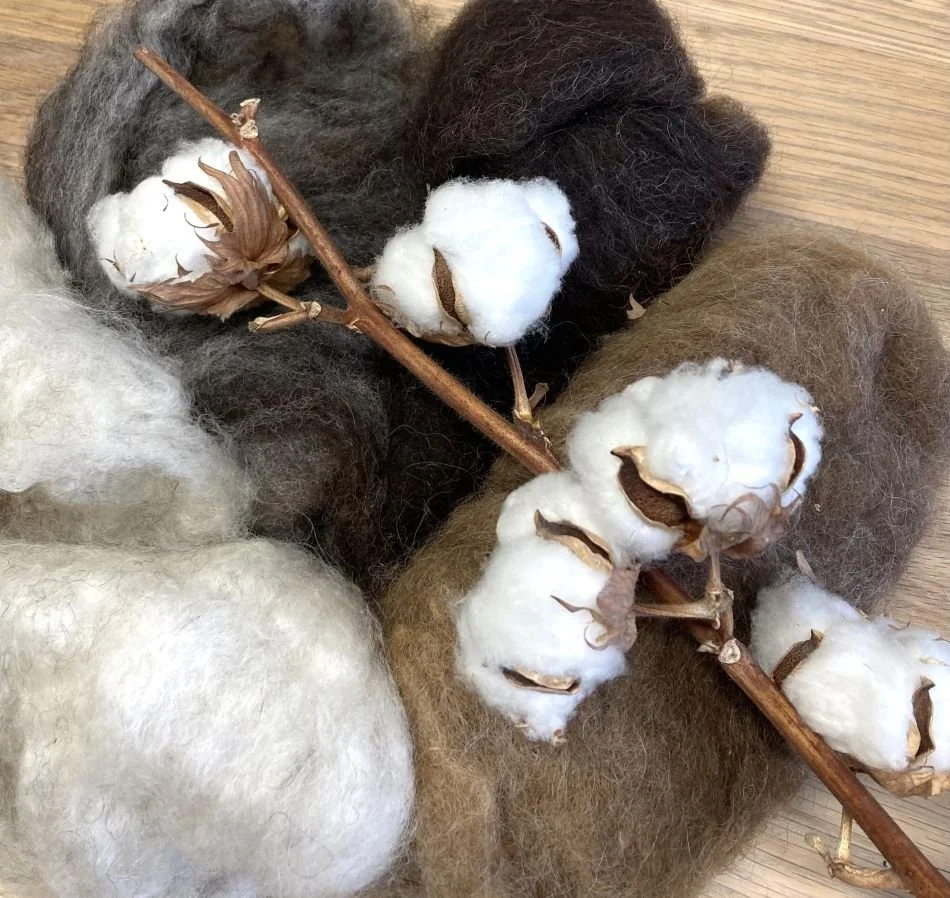 Puuvillapalloja ja -oksa eri väreissä, kuten valkoisia, harmaita, ruskeita ja mustia, aseteltuna pöydälle.