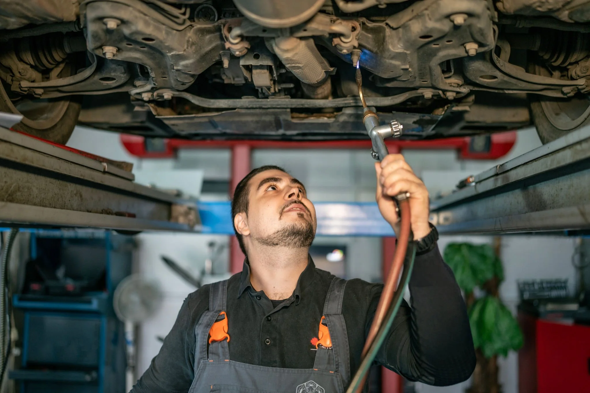 A mechanic working underneath a car raised on a lift, inspecting or repairing the vehicle's underside.