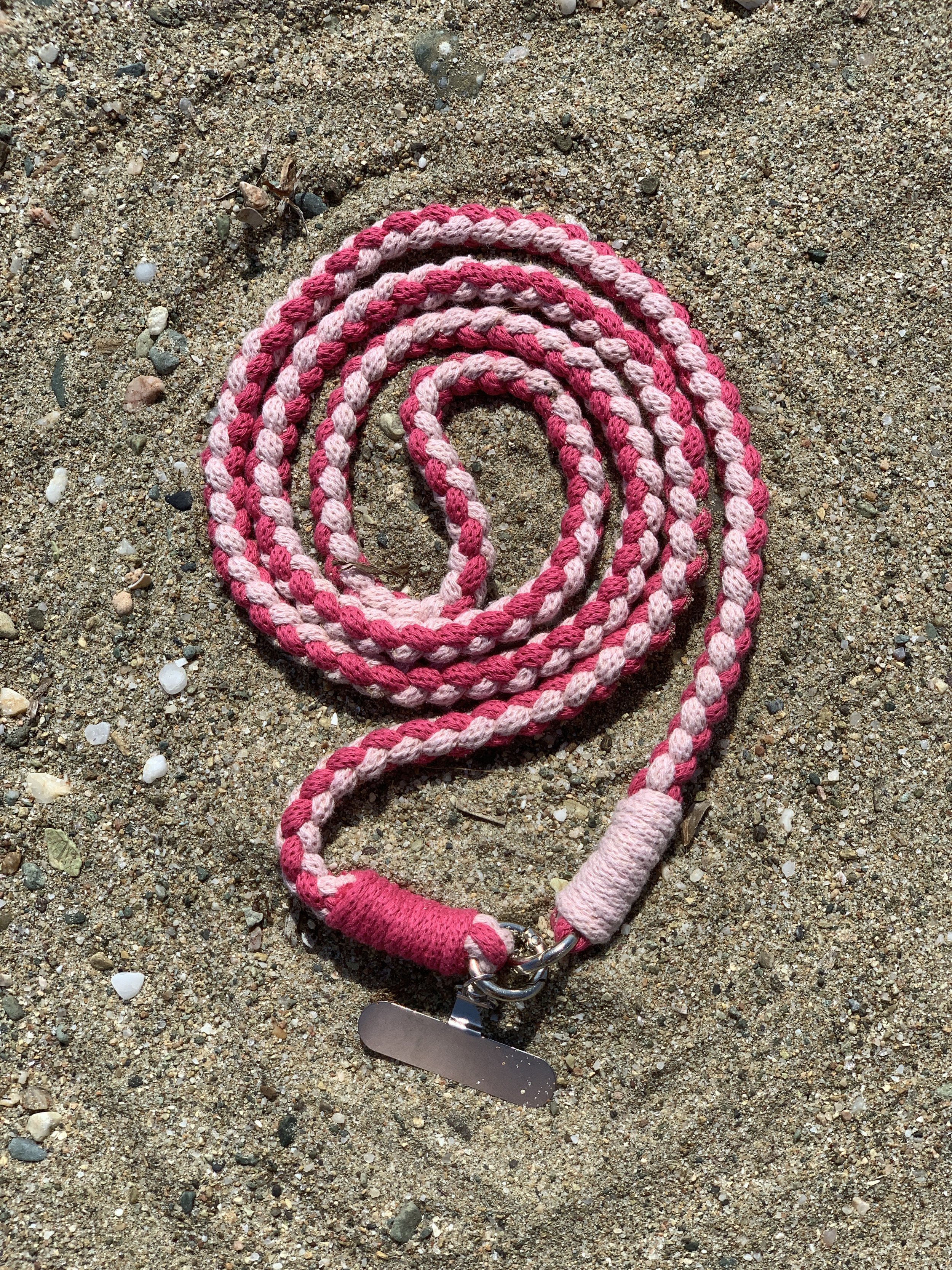 Rosa und hellrosa geflochtenes Hundehalsband liegt auf Sand am Strand.