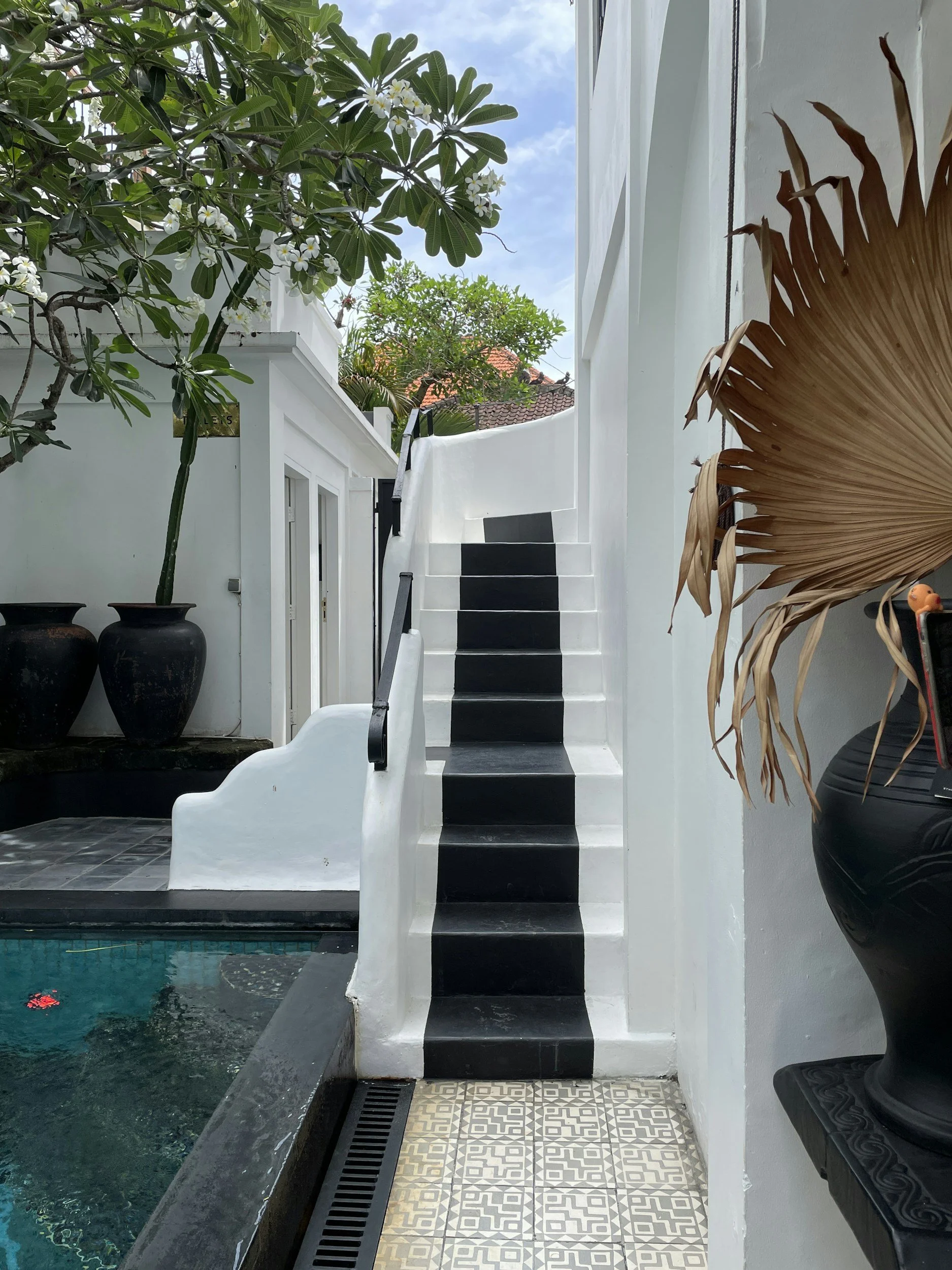 Escalier noir et blanc à côté de la piscine dans une cour intérieure avec des plantes et des pots en terre cuite.