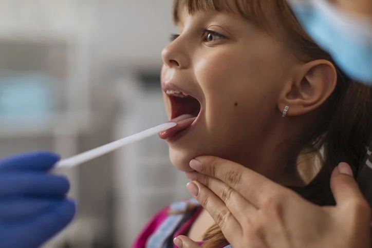 A young girl having her throat swab tested by a healthcare professional in a clinical setting.