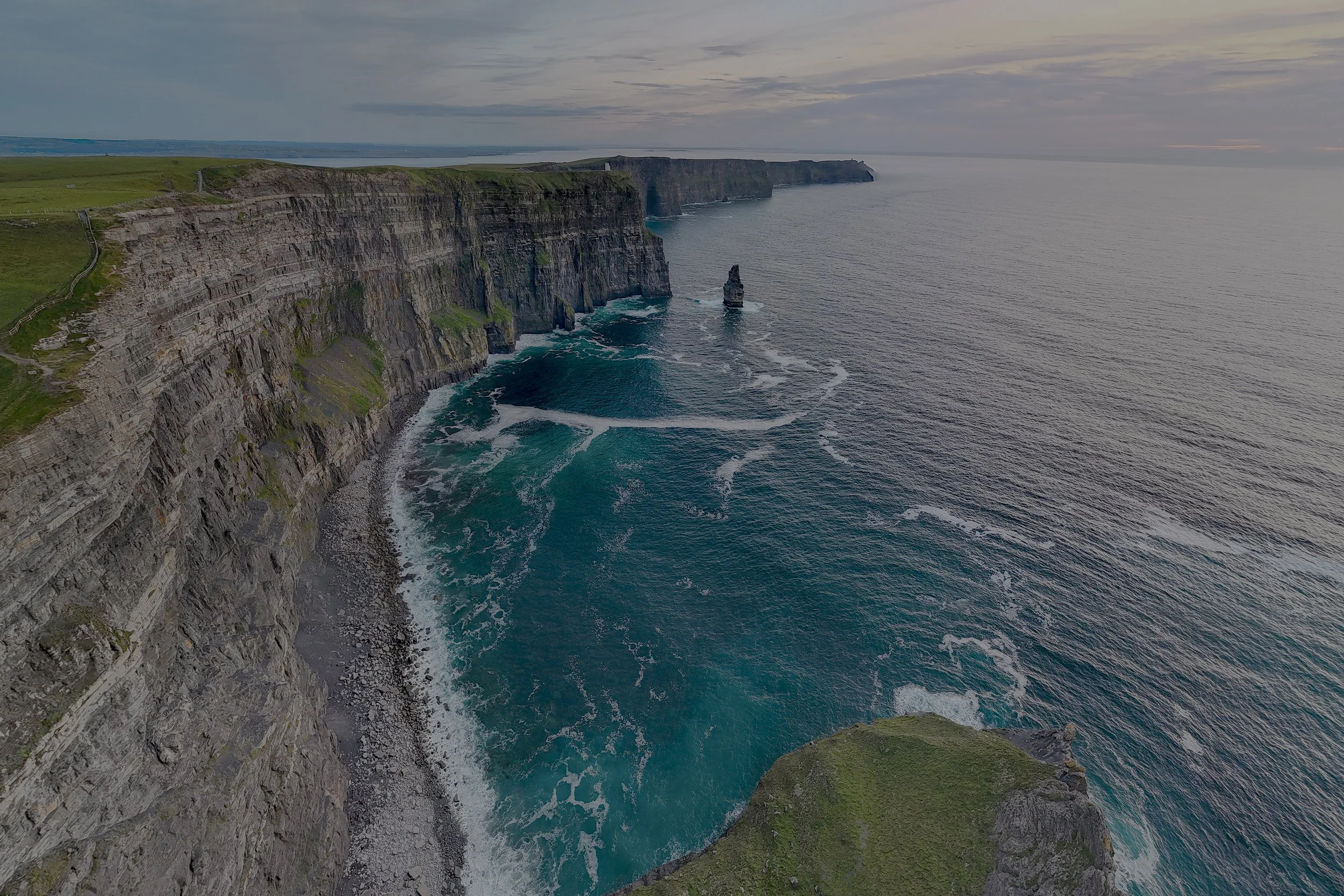 Aerial view of rugged chalk cliffs along the coast with a rock formation in the sea, under a cloudy sky.