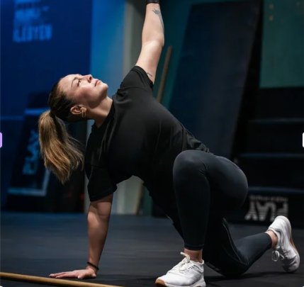 Woman in black activewear performing a stretch or exercise on the floor in a gym.