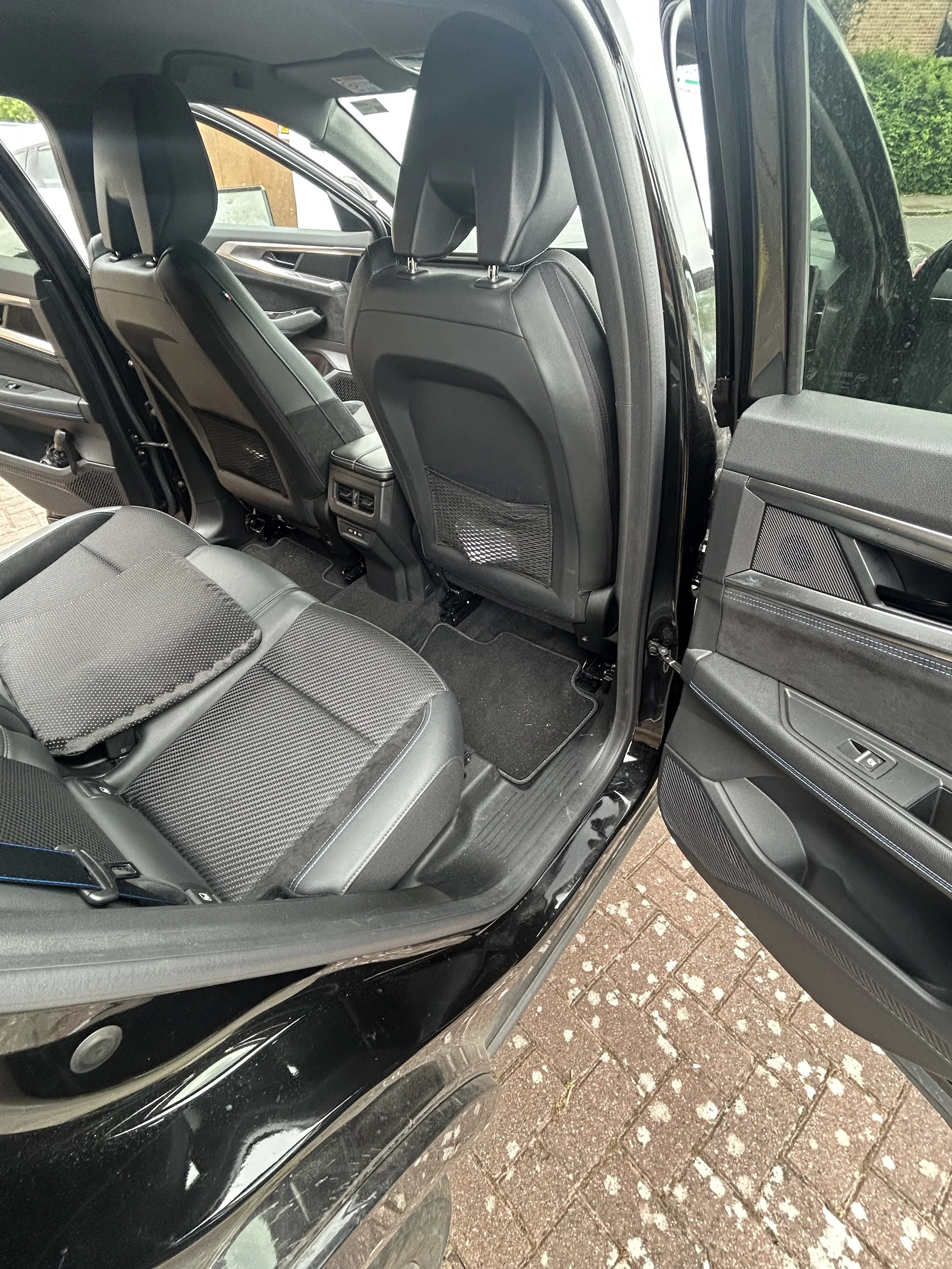 The interior of a black SUV showing black leather seats, headrests, and rear storage pockets, with a view of the front seats and dashboard through the open door.